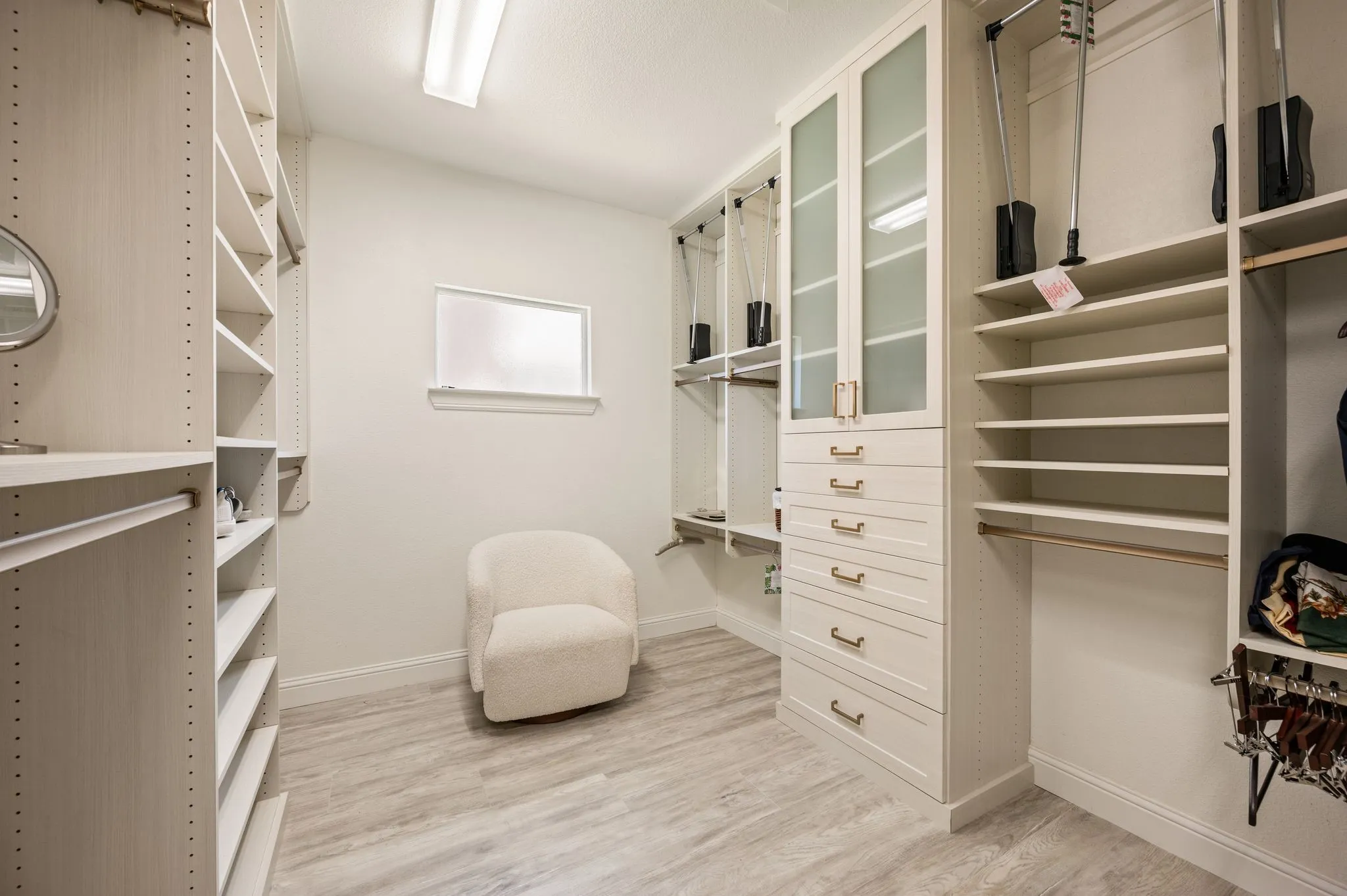 Luxurious custom walk-in closet featuring custom cabinetry with glass-front doors, multiple built-in shelving units, and coordinating drawer storage