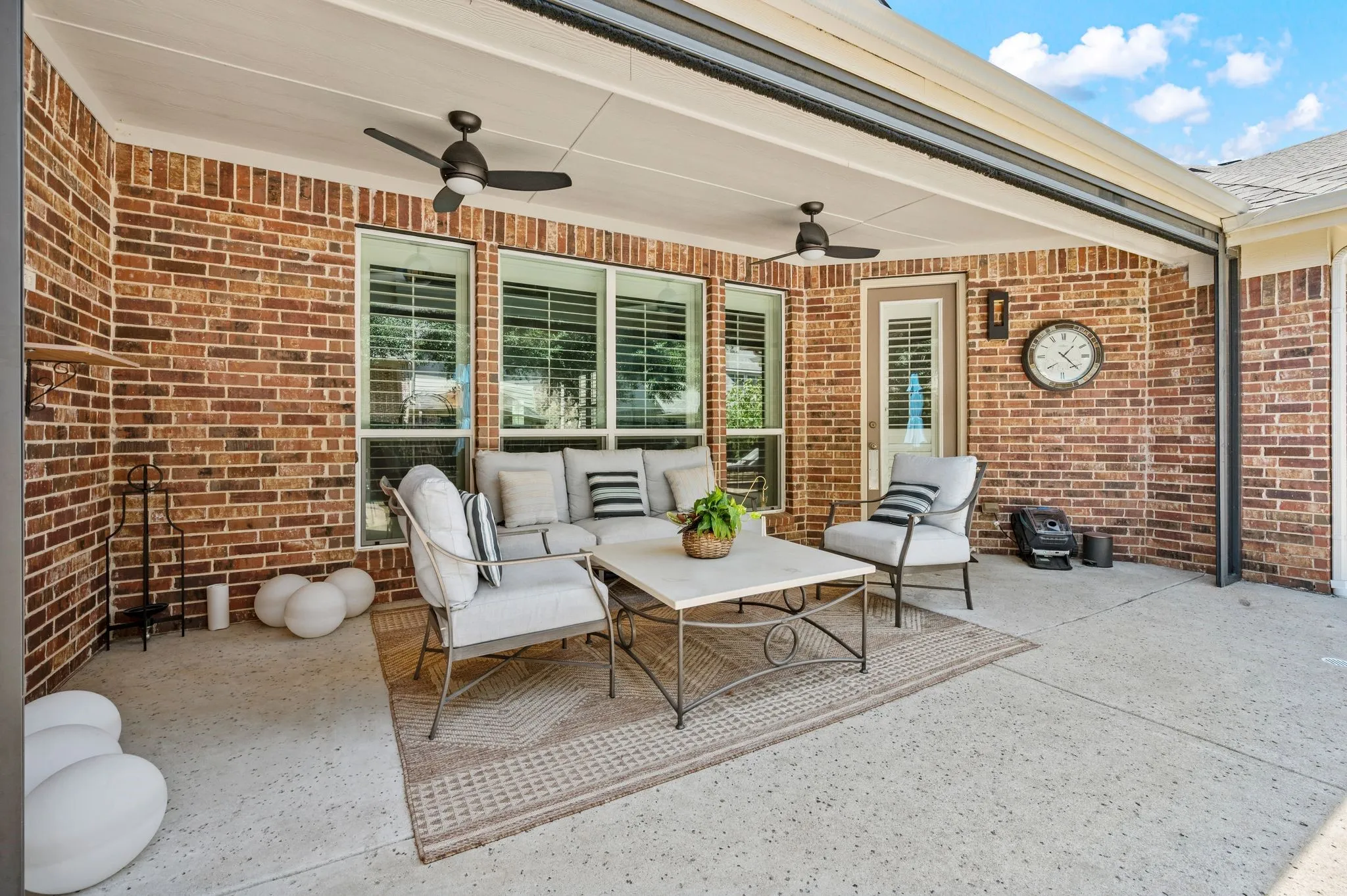 Covered patio featuring a brick exterior, concrete flooring, and two ceiling fans