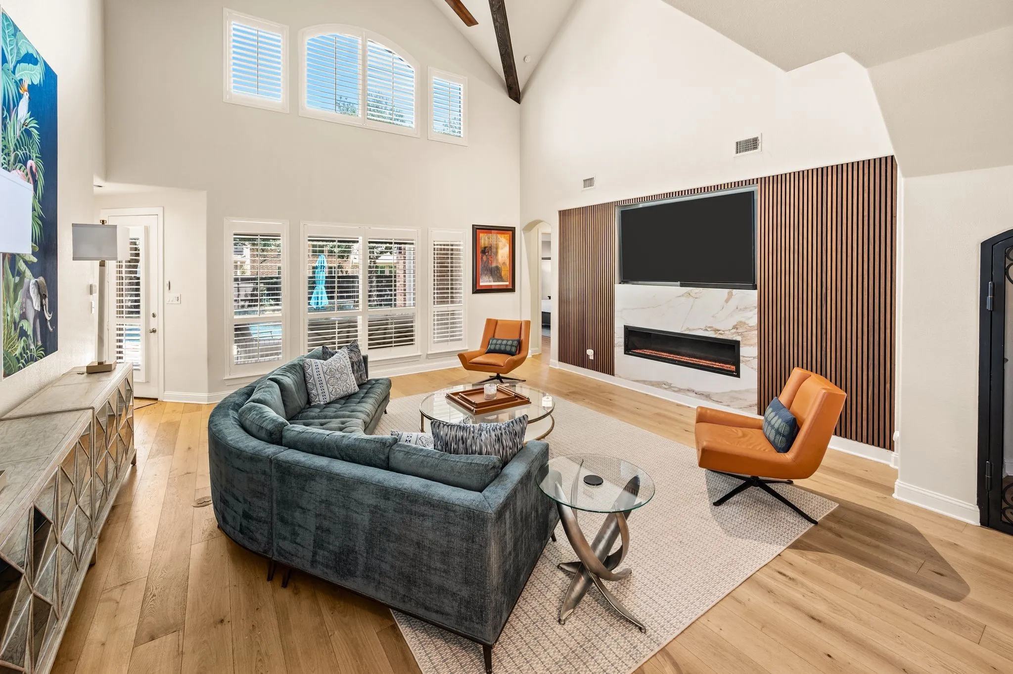 Vaulted ceiling with exposed beam, wood flooring, accent fireplace wall with integrated linear fireplace, marble-finish surround, and wood paneling