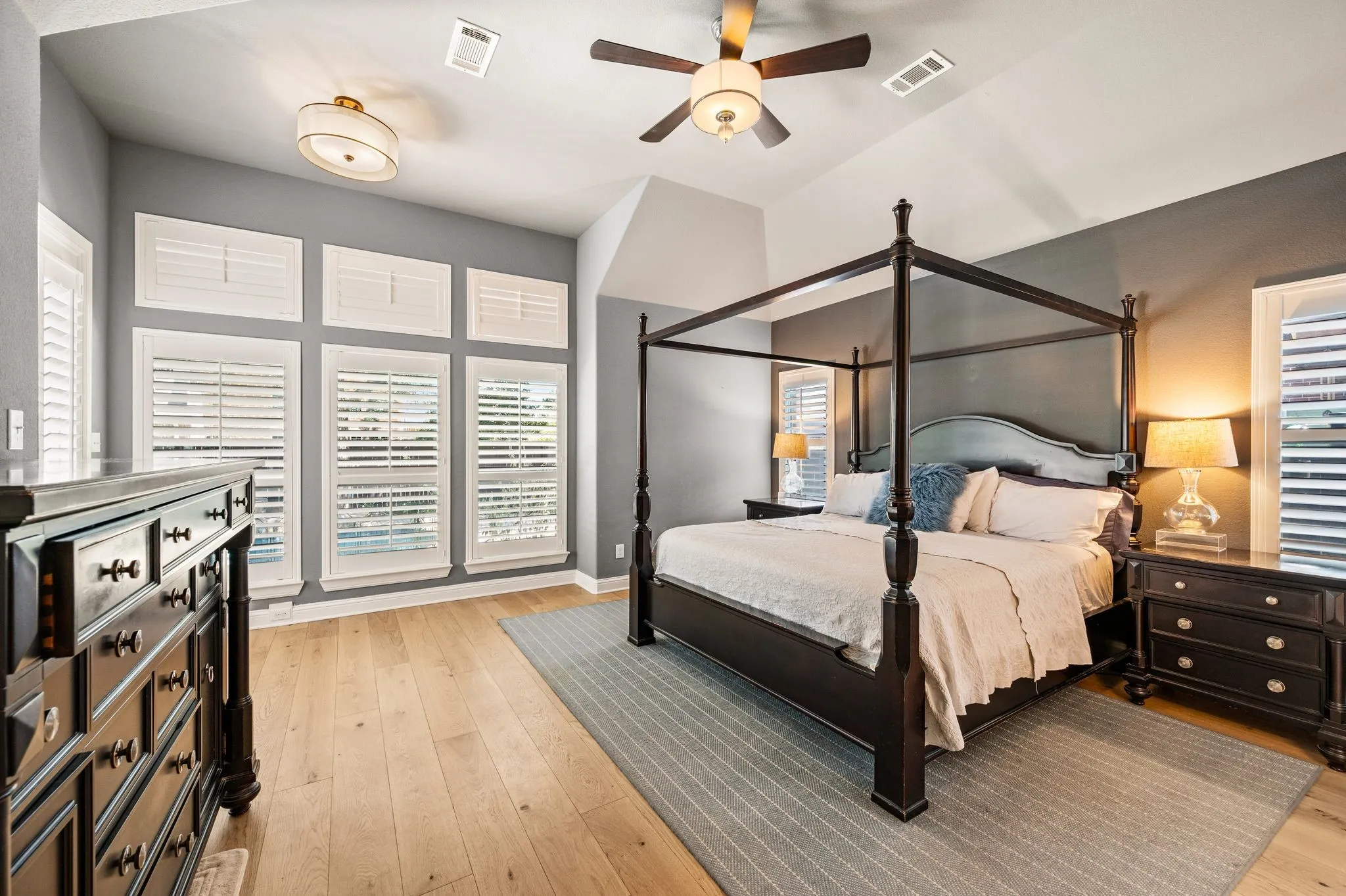 Vaulted ceiling with a ceiling fan, light wood flooring, and white plantation shutters on multiple windows