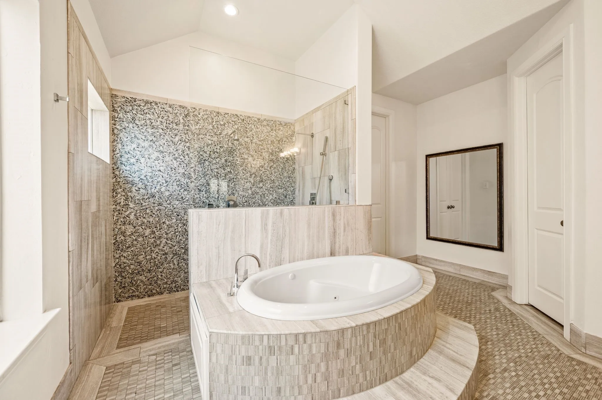 Oval soaking tub set in a tiled surround, glass-enclosed shower with mosaic wall tile, and coordinating mosaic floor tile