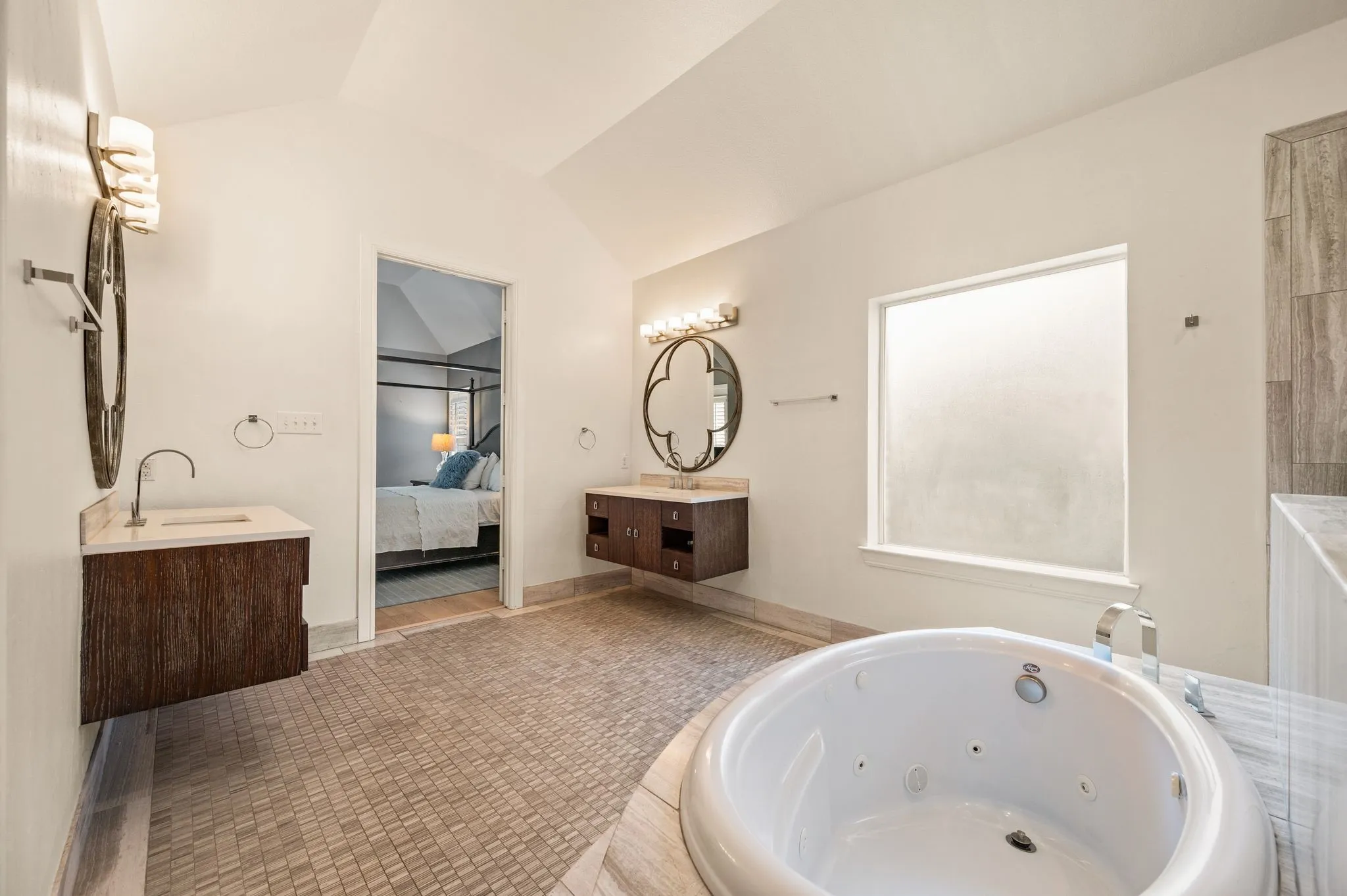 Soaking tub with deck-mounted faucet, dual floating vanities with countertop sinks, and wall-mounted light fixtures