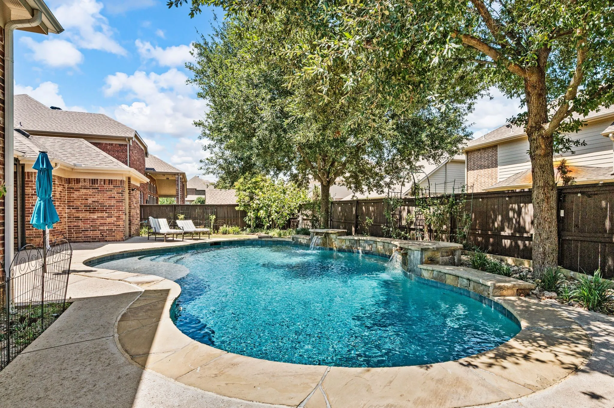 Custom-shaped swimming pool with integrated waterfalls, and ample surrounding hardscaping