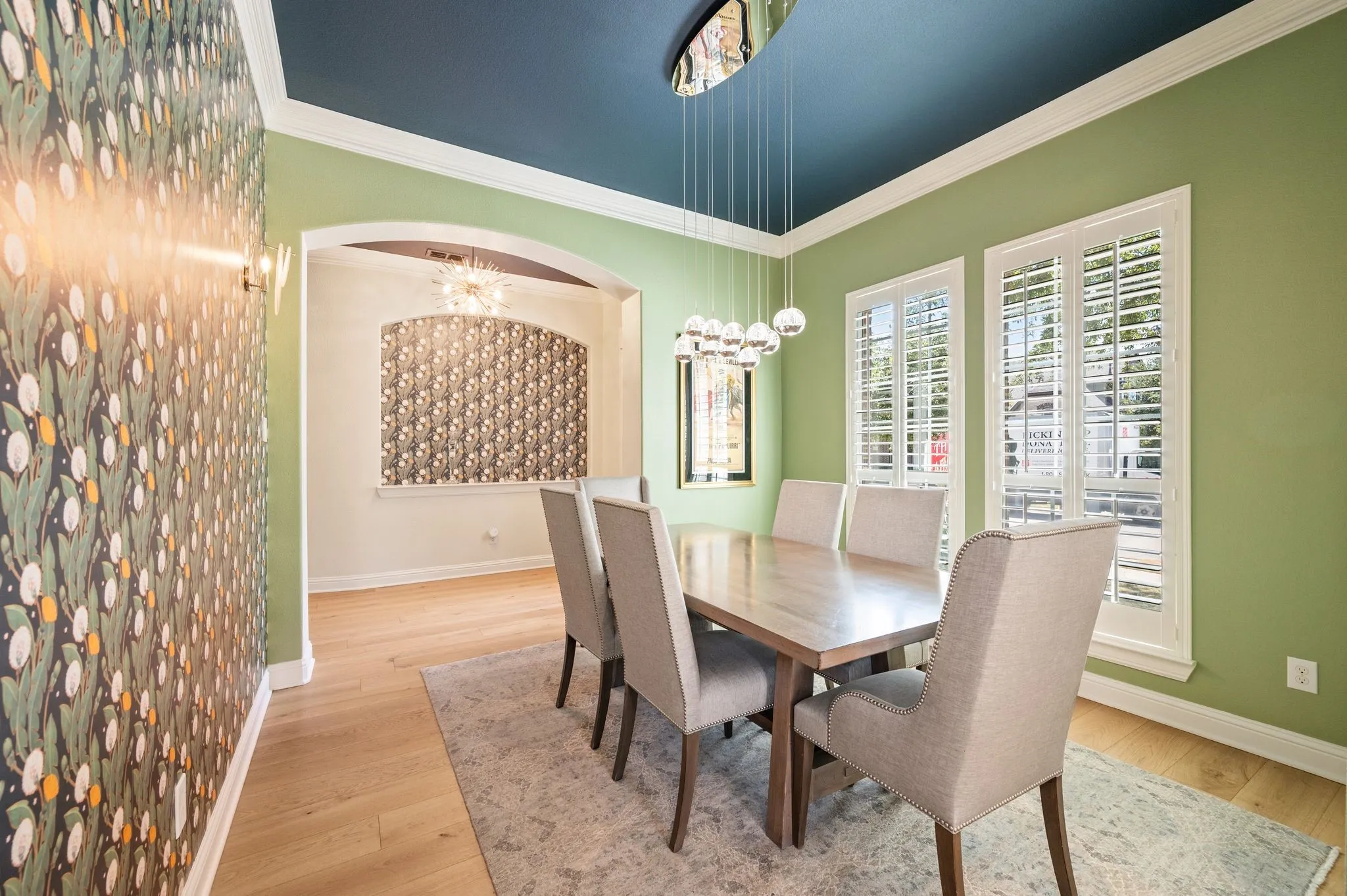 Dining area with wood flooring, two large windows featuring white plantation shutters, and a dark-toned ceiling with a modern chandelier