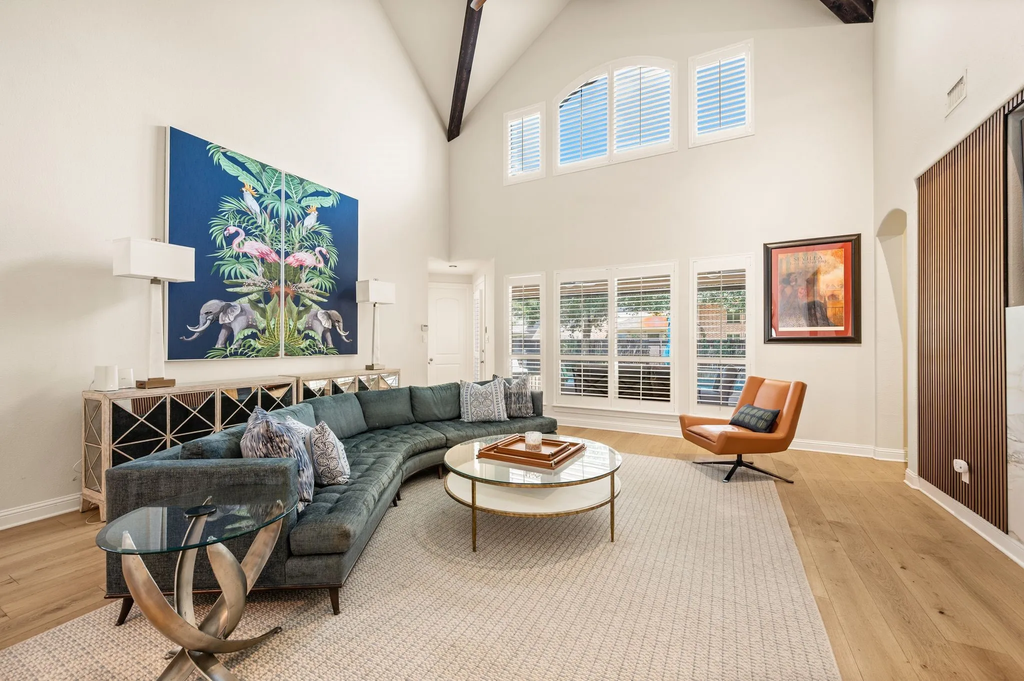 Vaulted ceilings with exposed beams, light wood flooring, and multiple arched windows with plantation shutters
