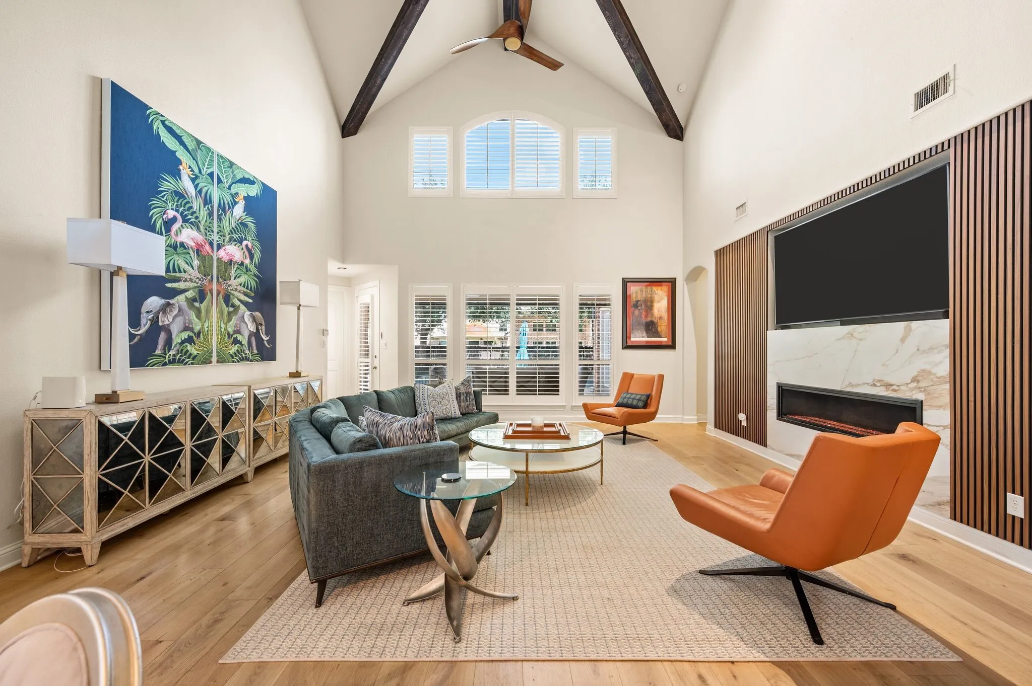 Vaulted ceilings with exposed beams, wood flooring, built-in electric fireplace with stone surround, custom wood accent wall, and arched transom windows