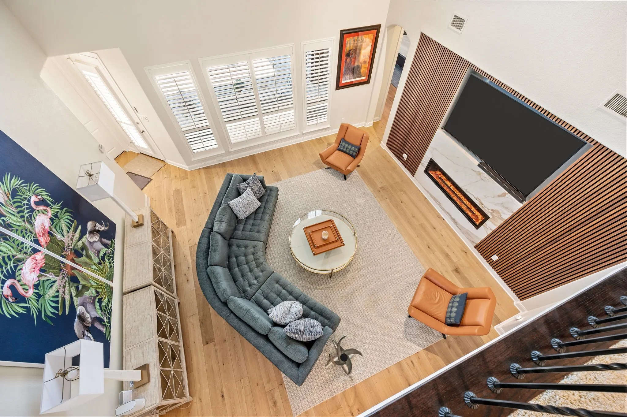 High ceilings with natural wood flooring, plantation shutters, and a modern linear fireplace with a wood-paneled accent wall