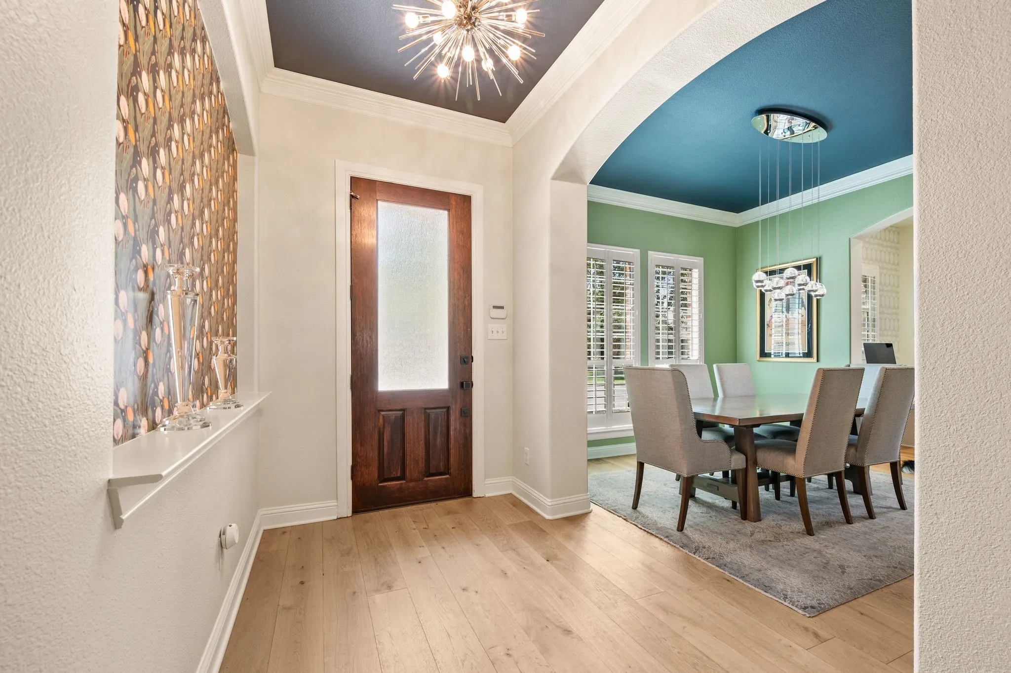 Light wood flooring throughout, solid wood entry door with frosted glass panel, recessed decorative wall niche, arched doorway, and plantation shutters