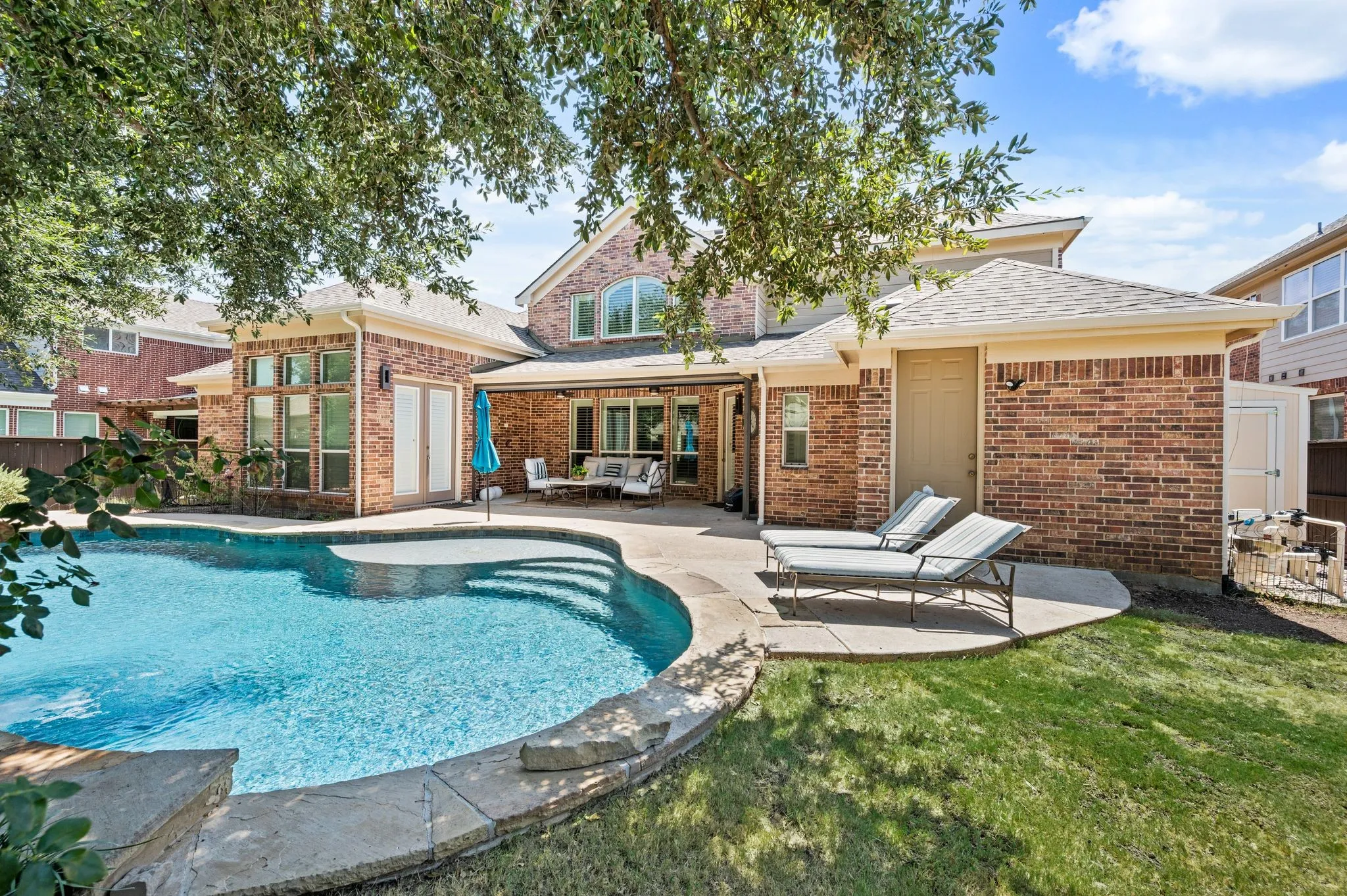 Expansive backyard featuring a curved swimming pool, stone coping, and a concrete deck.