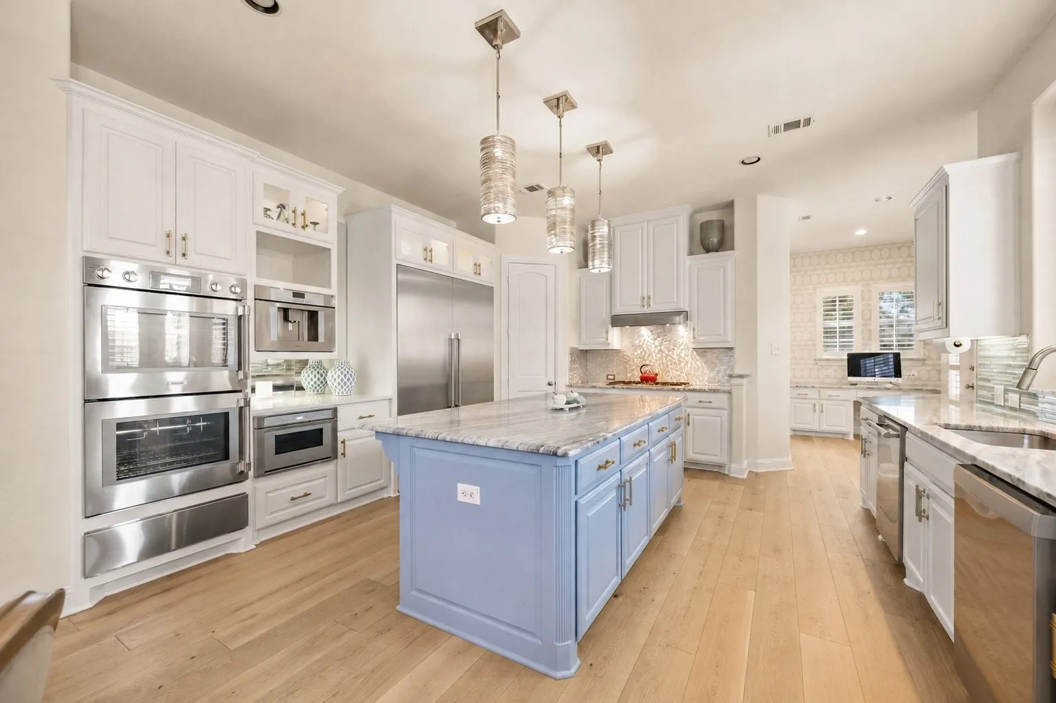 Kitchen featuring wood flooring, a light blue island with a marble countertop, white cabinetry, Thermador stainless steel appliances, and pendant lighting