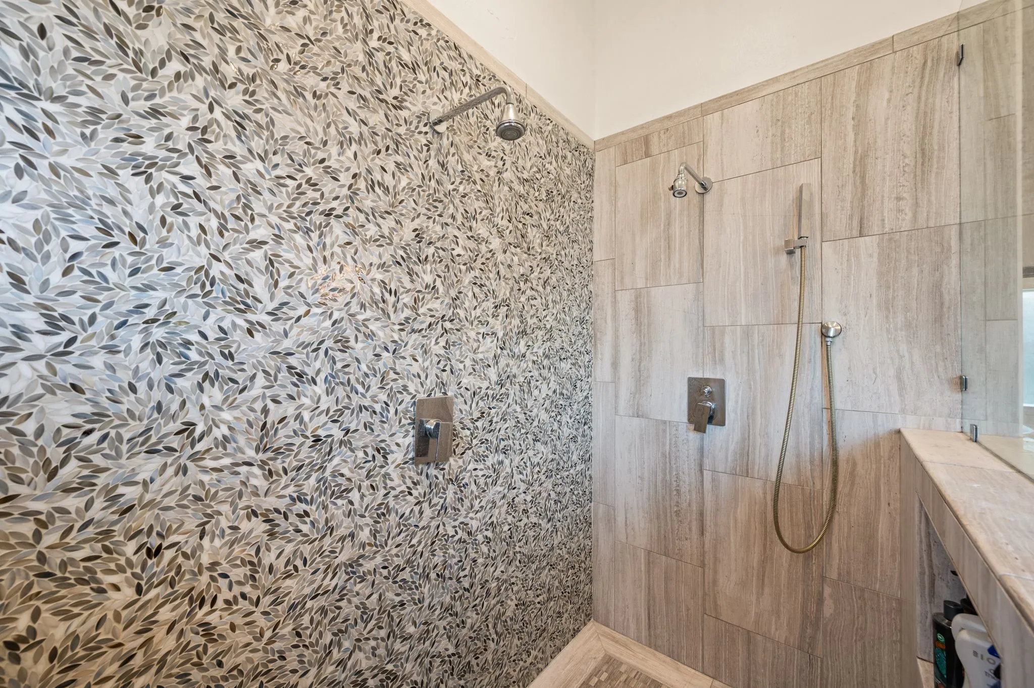 Shower stall featuring a unique mosaic tile wall, large format tile, fixed shower head, and an additional handheld shower fixture