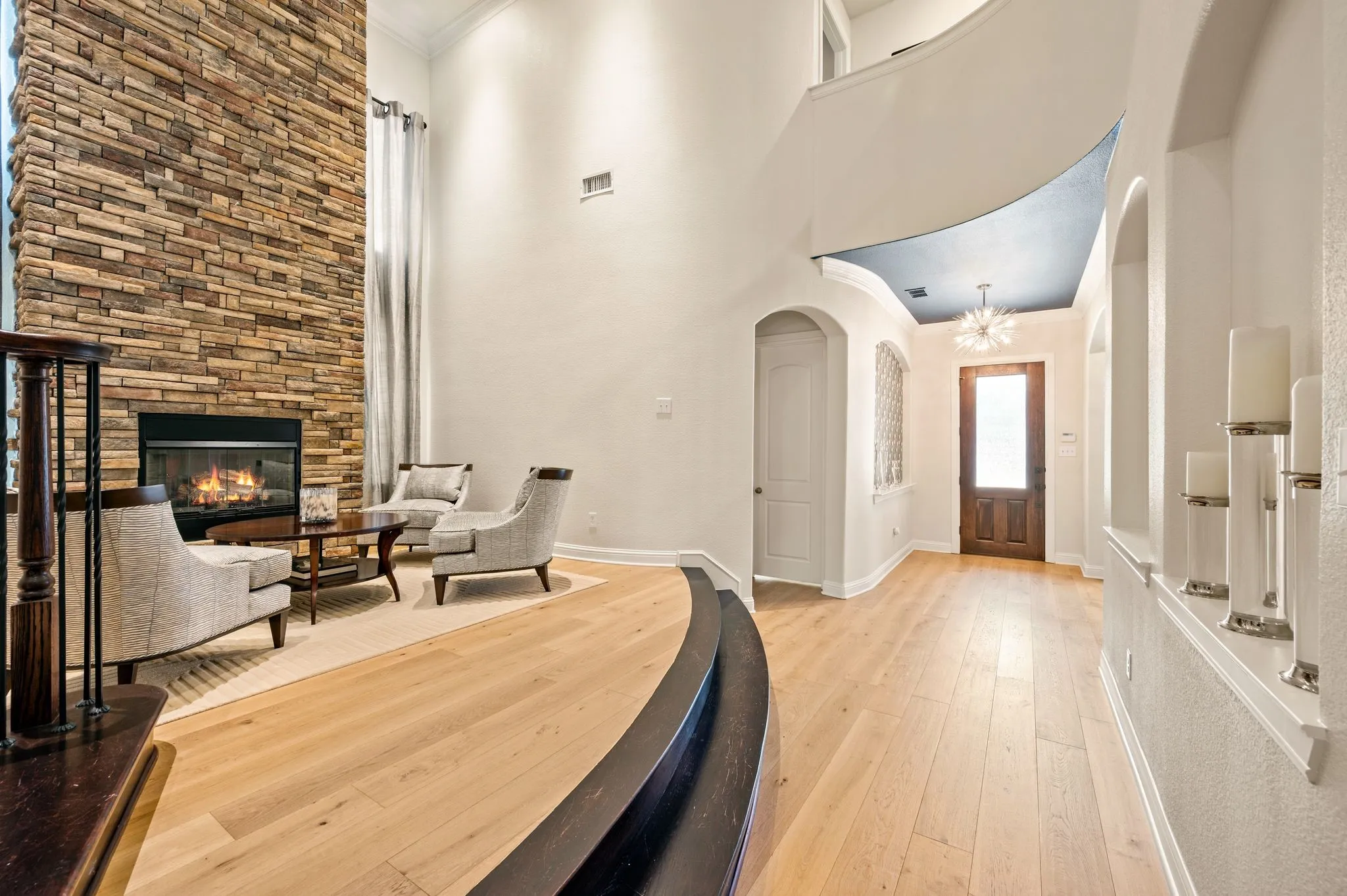 Wood flooring throughout, a stone-clad fireplace, a decorative front door with a transom window, and an arched entryway