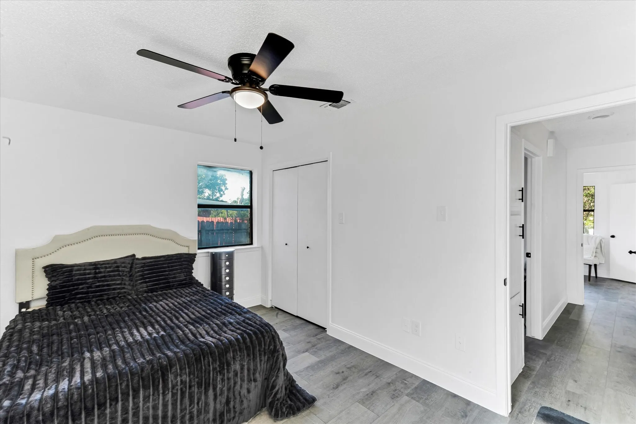 Black ceiling fan with integrated lighting, wood-look flooring, white walls, double bi-fold closet doors, and a window with exterior views