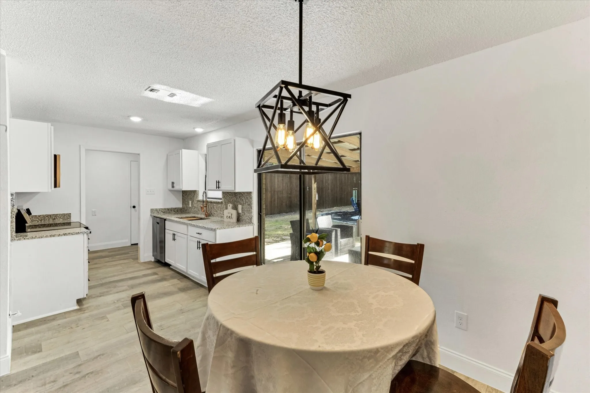 Open-concept kitchen and dining area featuring a modern geometric chandler, white cabinetry, and granite countertops