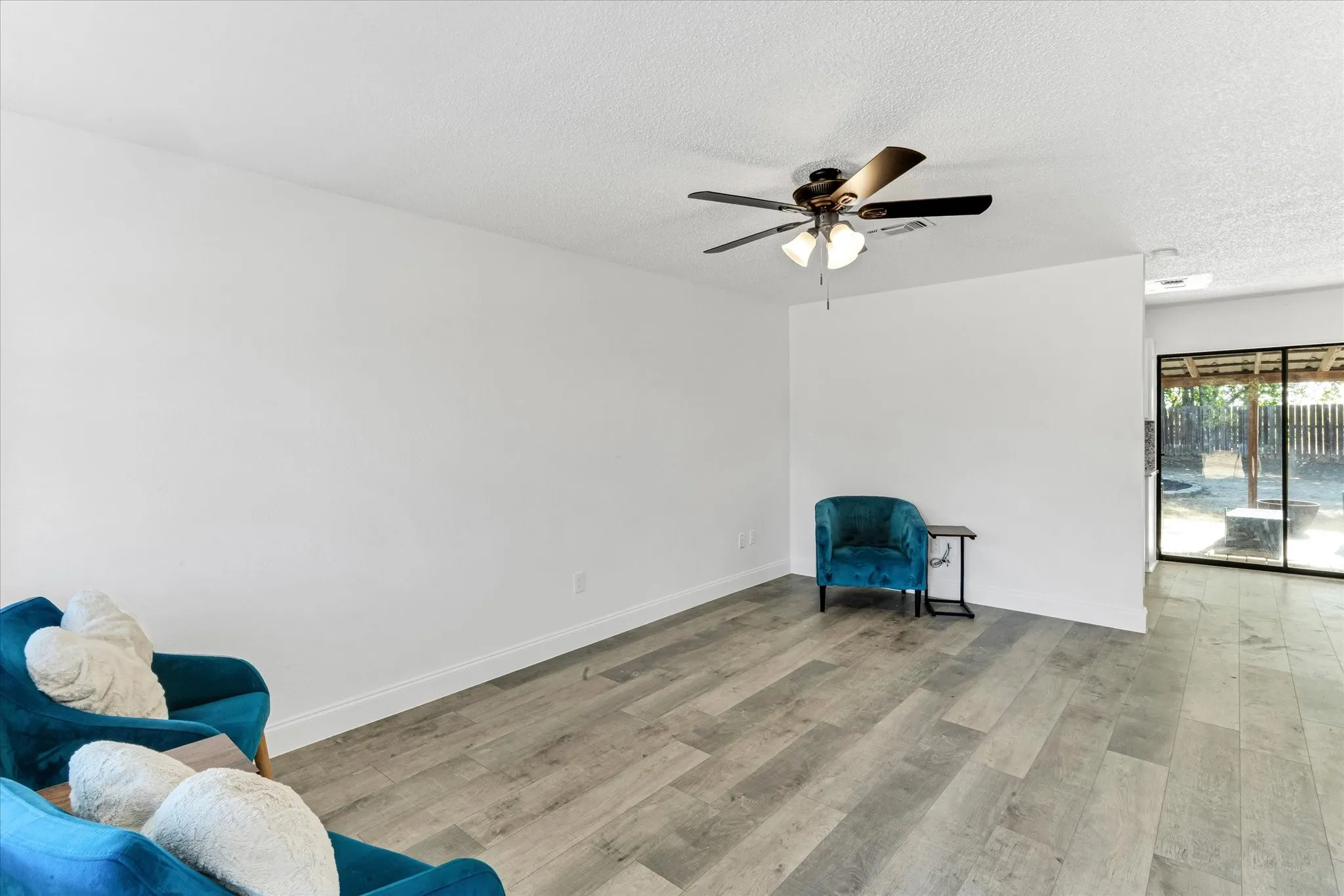 Wood-finish flooring, ceiling fan with integrated lighting, white walls, and sliding glass door to exterior