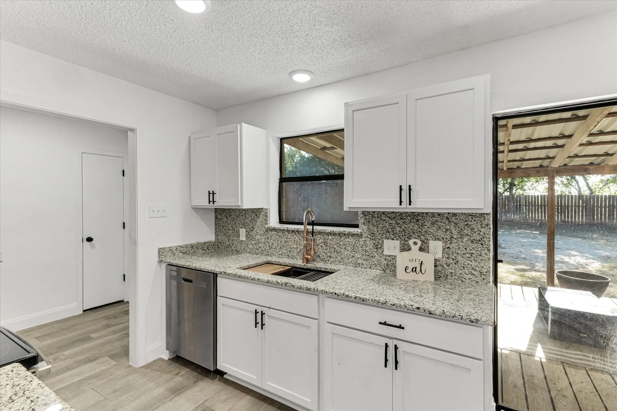 White cabinetry with matte black hardware, granite countertops with matching backsplash, new stainless steel dishwasher, and wood-finish flooring
