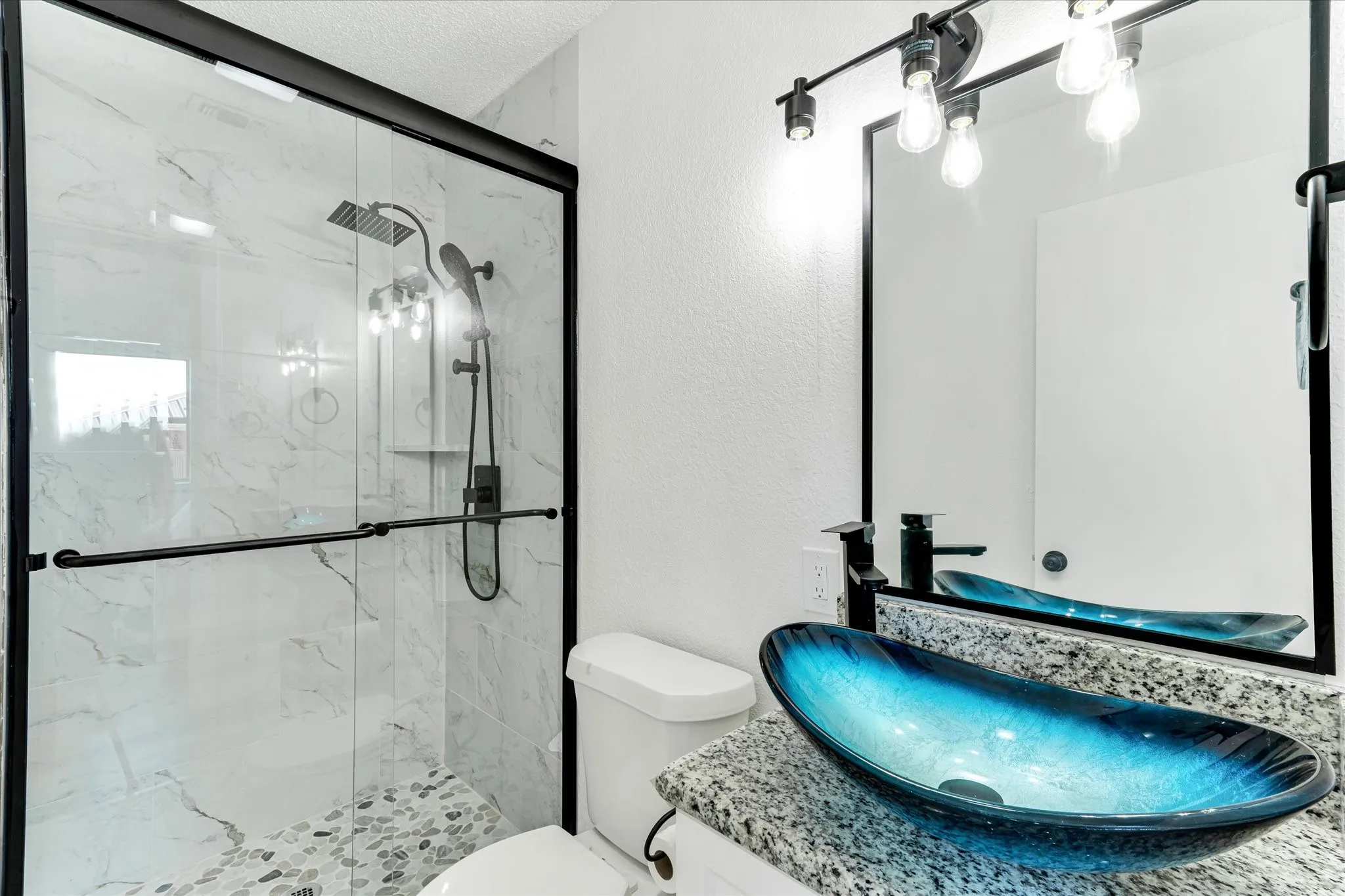 Glass-enclosed shower with a rainfall showerhead, pebble tile flooring, and white marble-patterned wall tiles