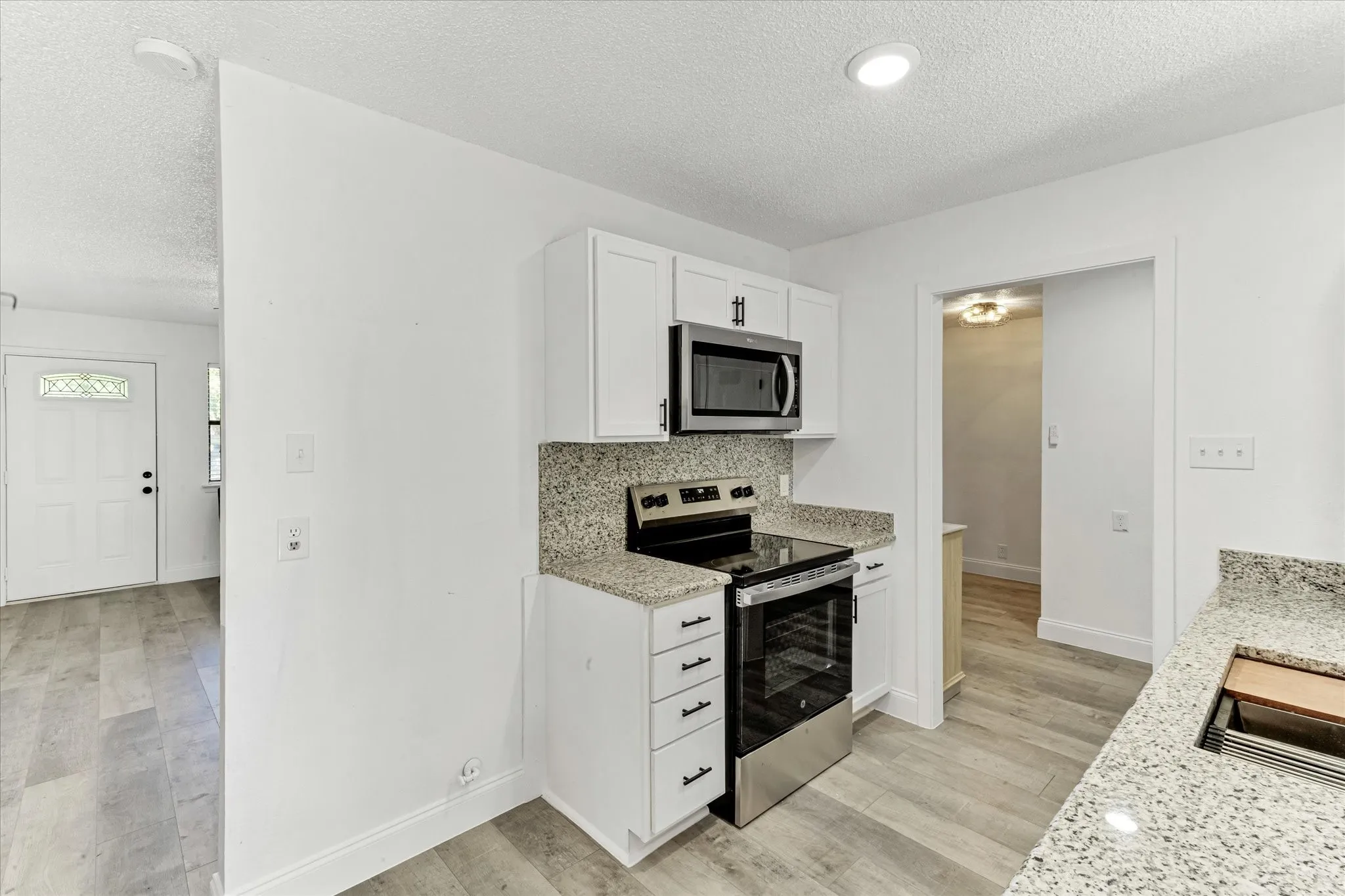 White cabinetry with dark hardware, new stainless steel appliances, speckled granite countertops, and wood-finish flooring