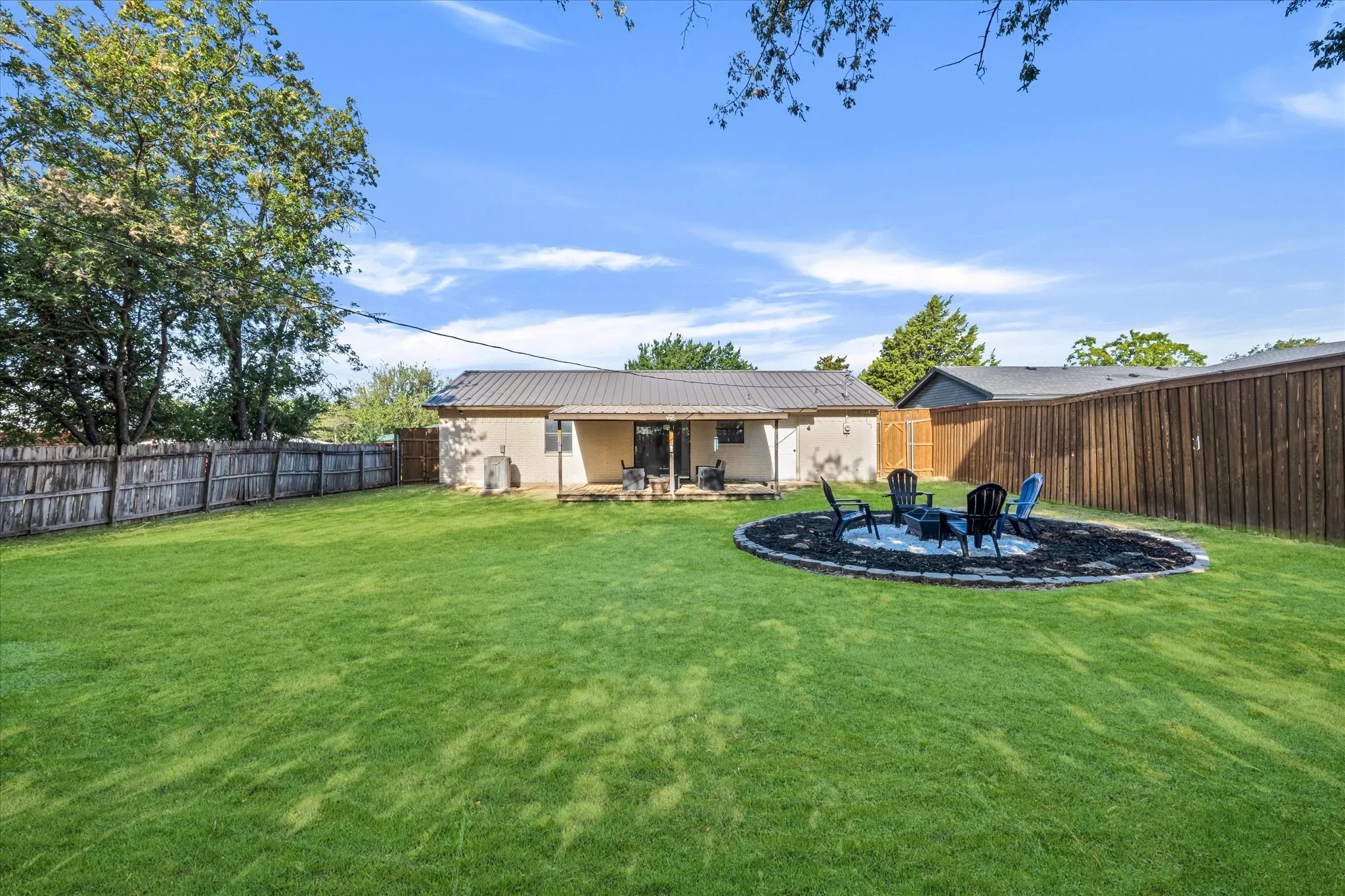 Expansive grassy yard with a stone-edged fire pit area, private wood fencing, and a covered back patio