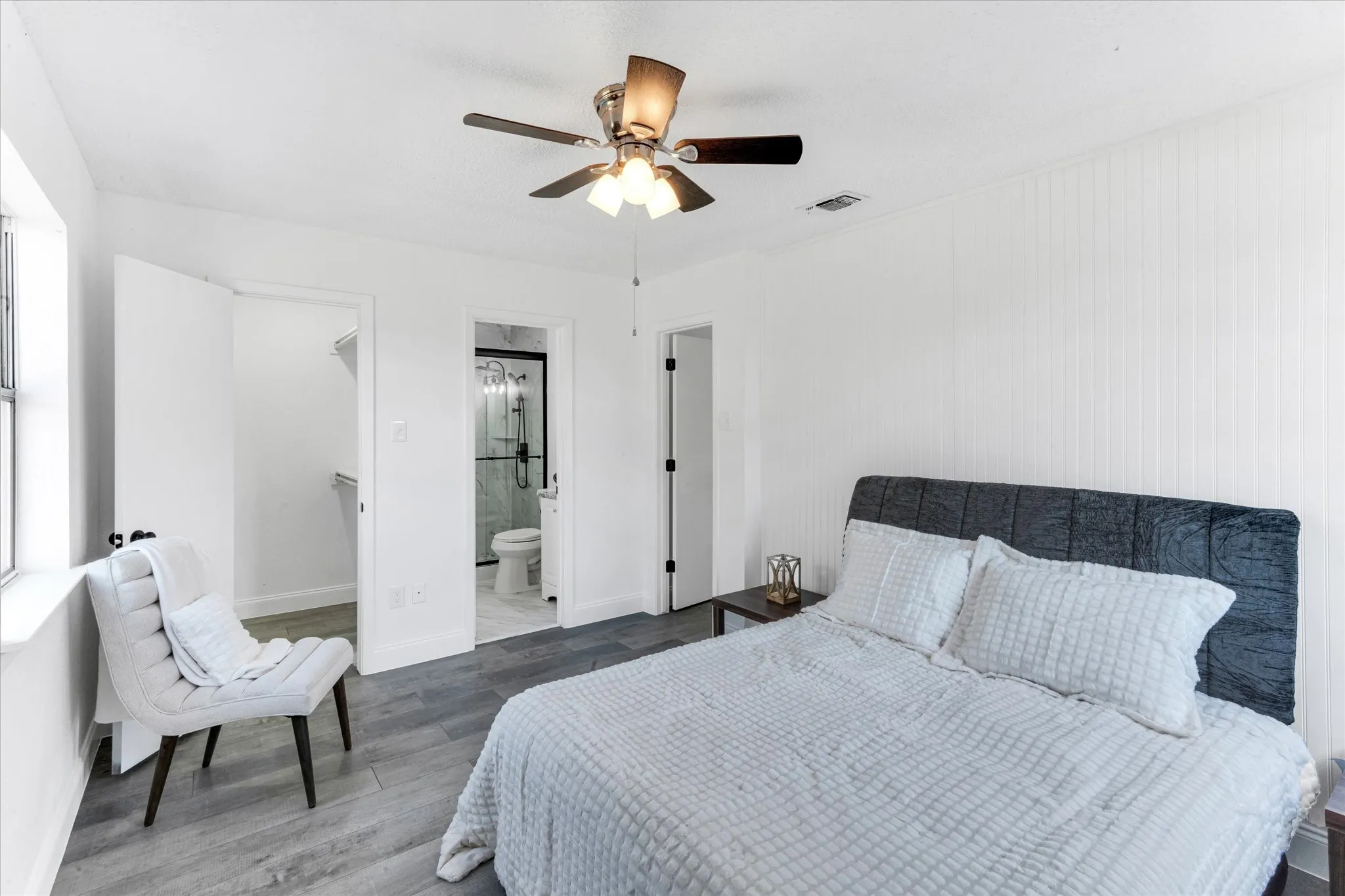 Wood-finish flooring, ceiling fan with integrated lighting, beadboard accent wall, walk-in closet, and an attached bathroom with a glass-enclosed shower