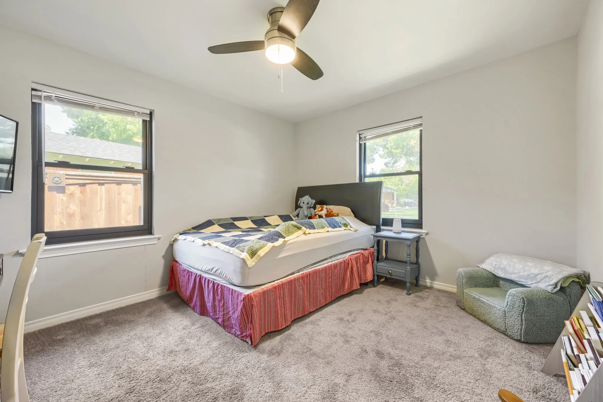 Light gray painted walls, carpet flooring, a ceiling fan with integrated lighting, and two windows with blinds