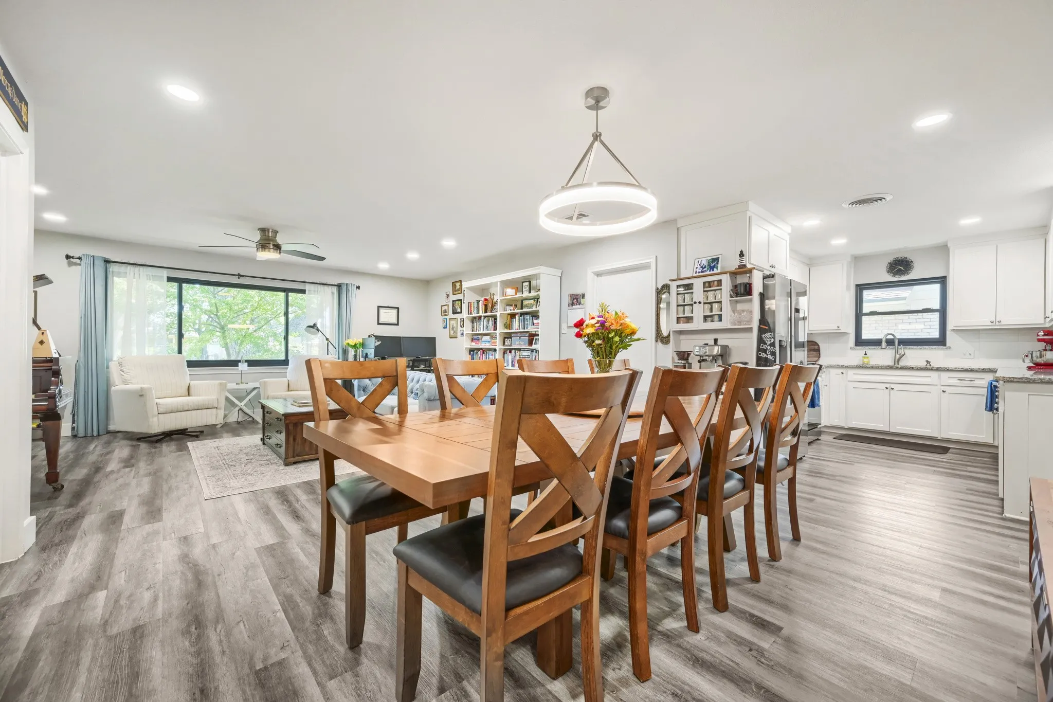 Open-concept living space featuring wood-finish flooring, recessed lighting, a modern chandelier, white cabinetry, and a large window