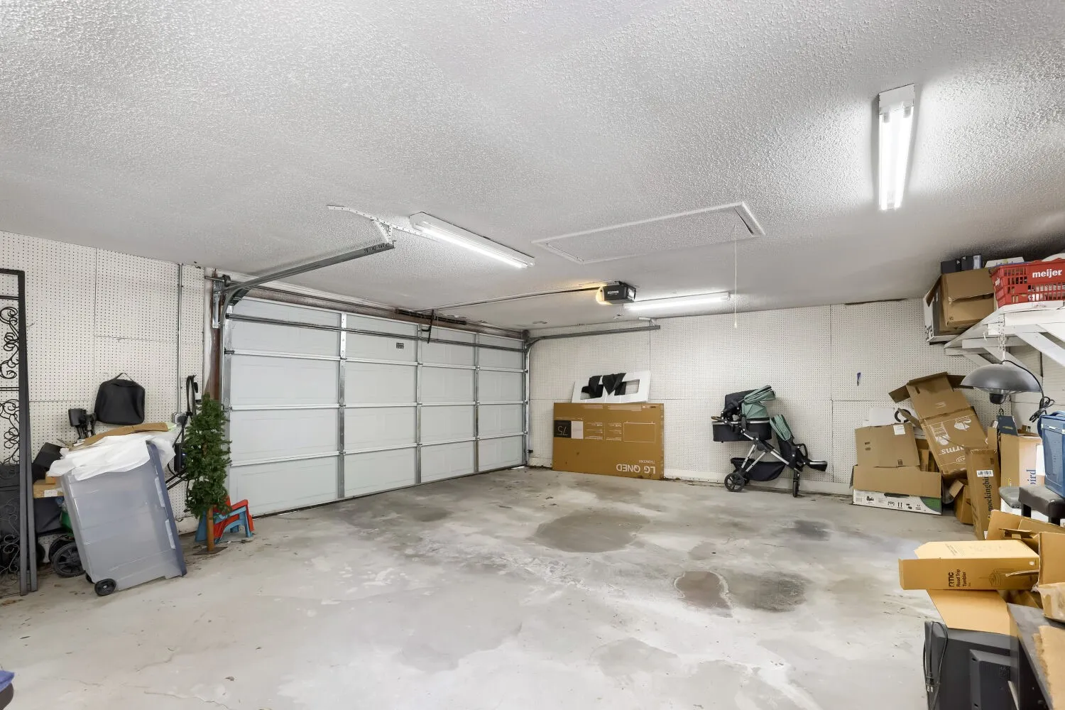 Concrete flooring, fluorescent ceiling lighting, white panel garage door, storage shelving, and a garage door opener system