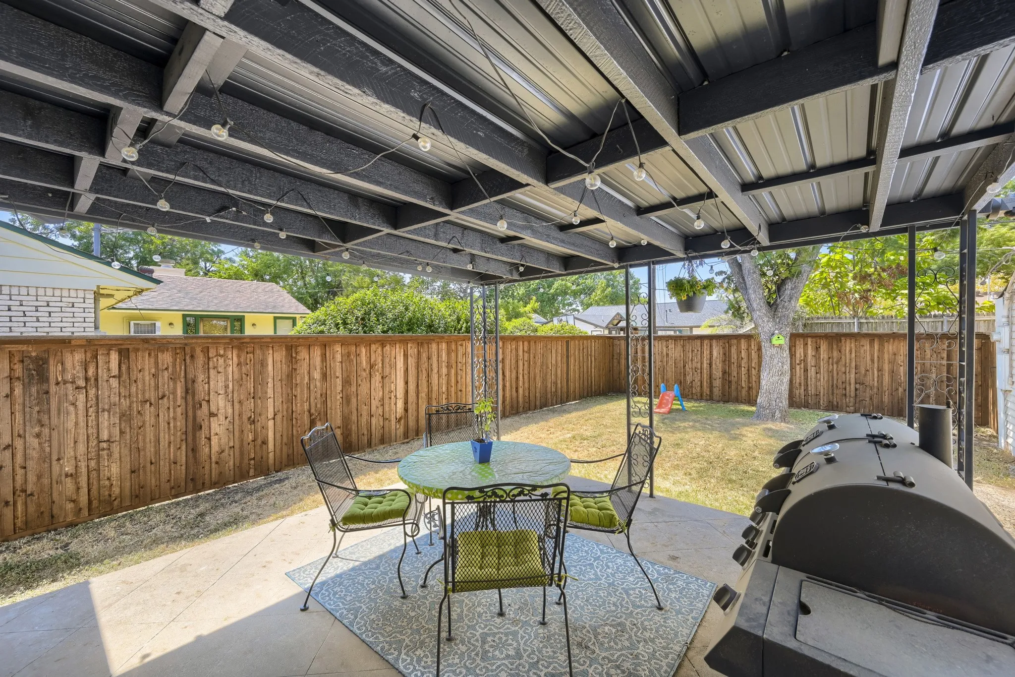 Covered patio with string lighting, concrete flooring, and a wood privacy fence