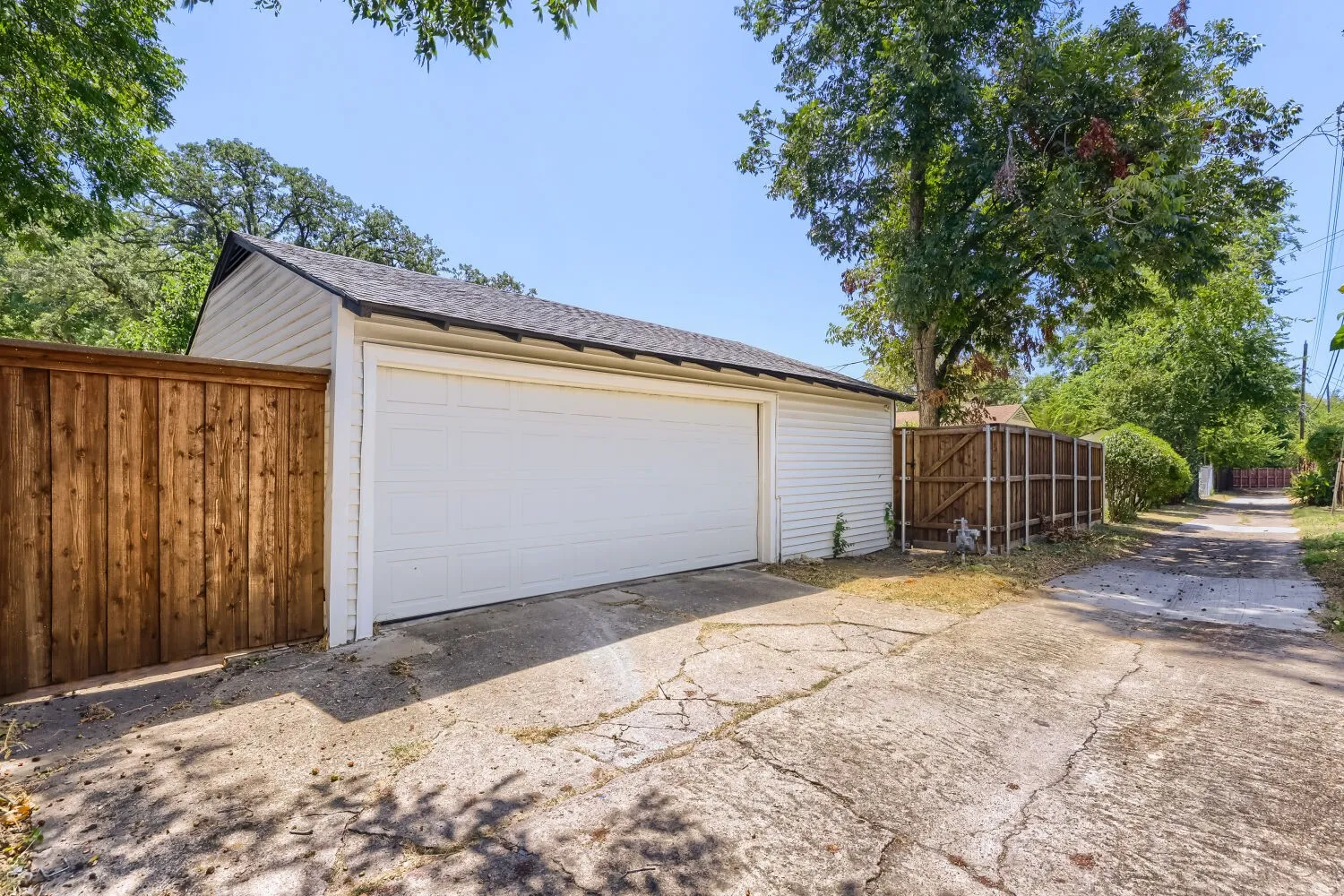 Detached garage featuring white siding and a shingle roof, accompanied by a wood privacy fence