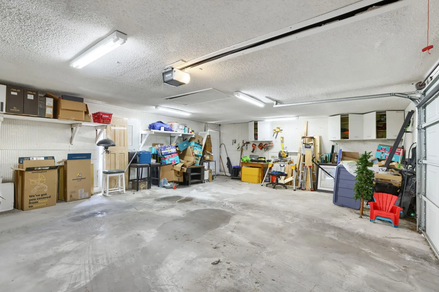 Garage featuring a concrete floor, fluorescent lighting, built-in shelving, and white cabinetry