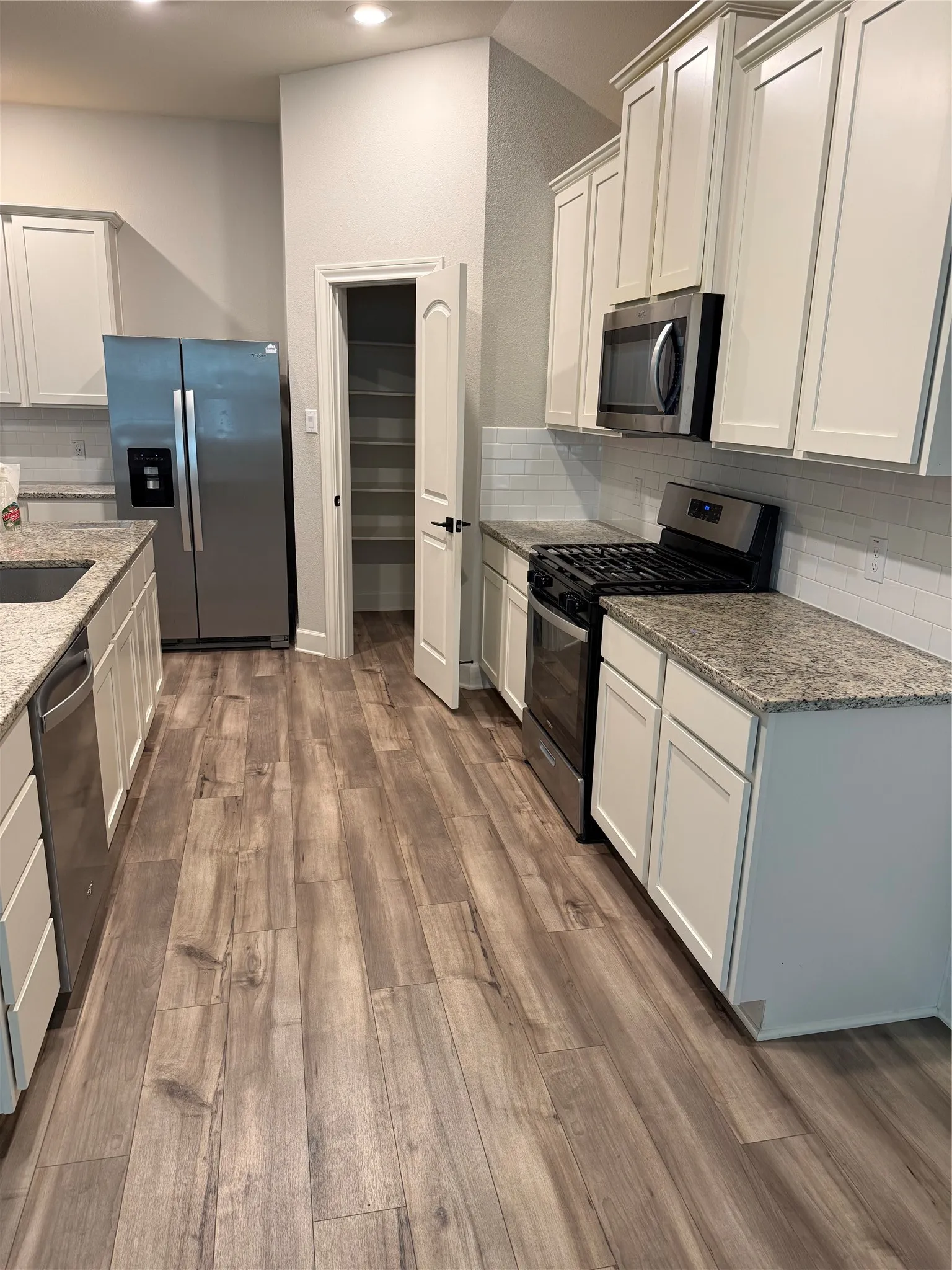 Kitchen with wood-finish flooring, white cabinetry, integrated stainless steel appliances, speckled countertops, and a subway tile backsplash