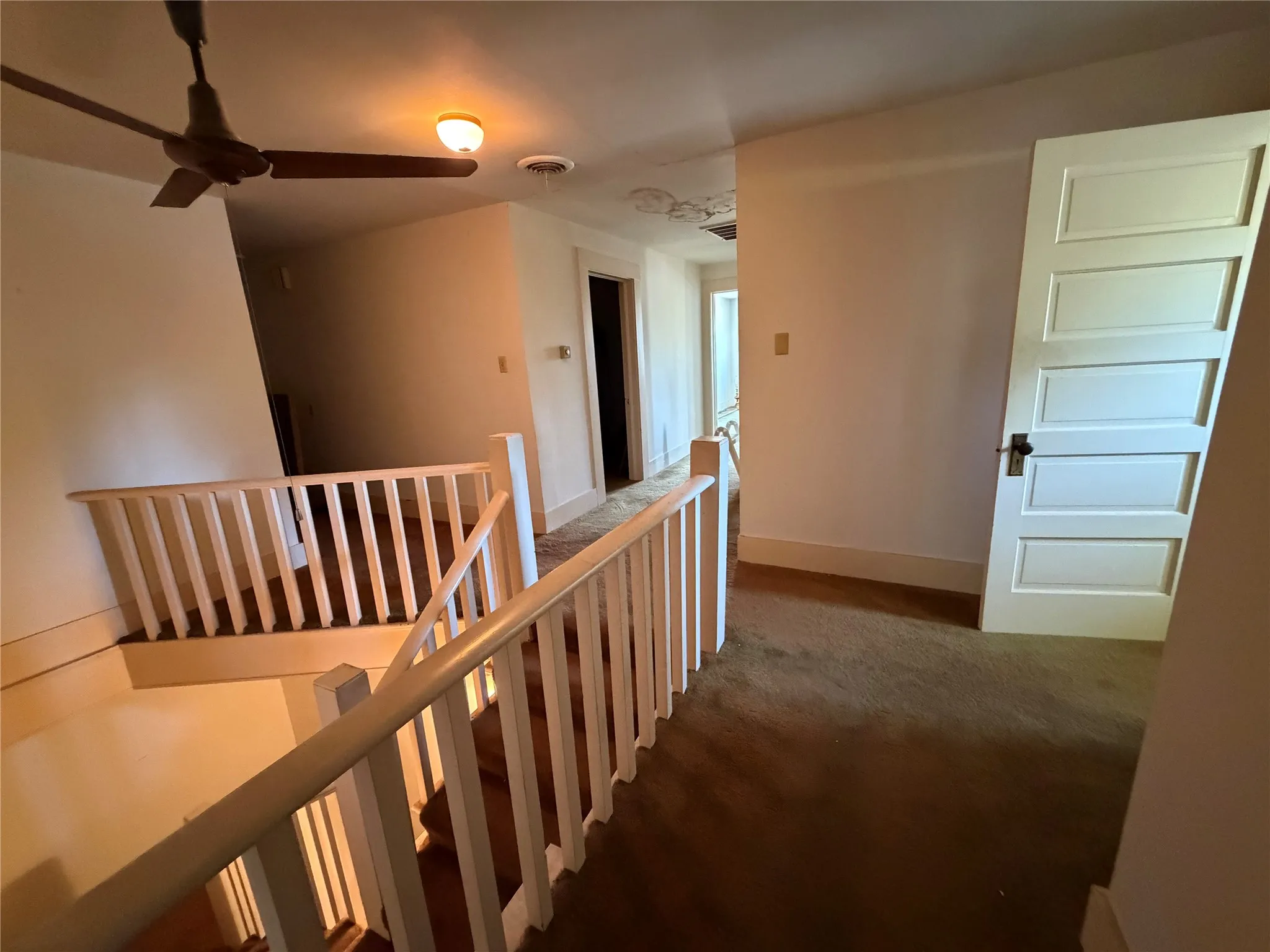 Staircase with painted wood balusters and railing, ceiling fan with integrated lighting, and a five-panel interior door