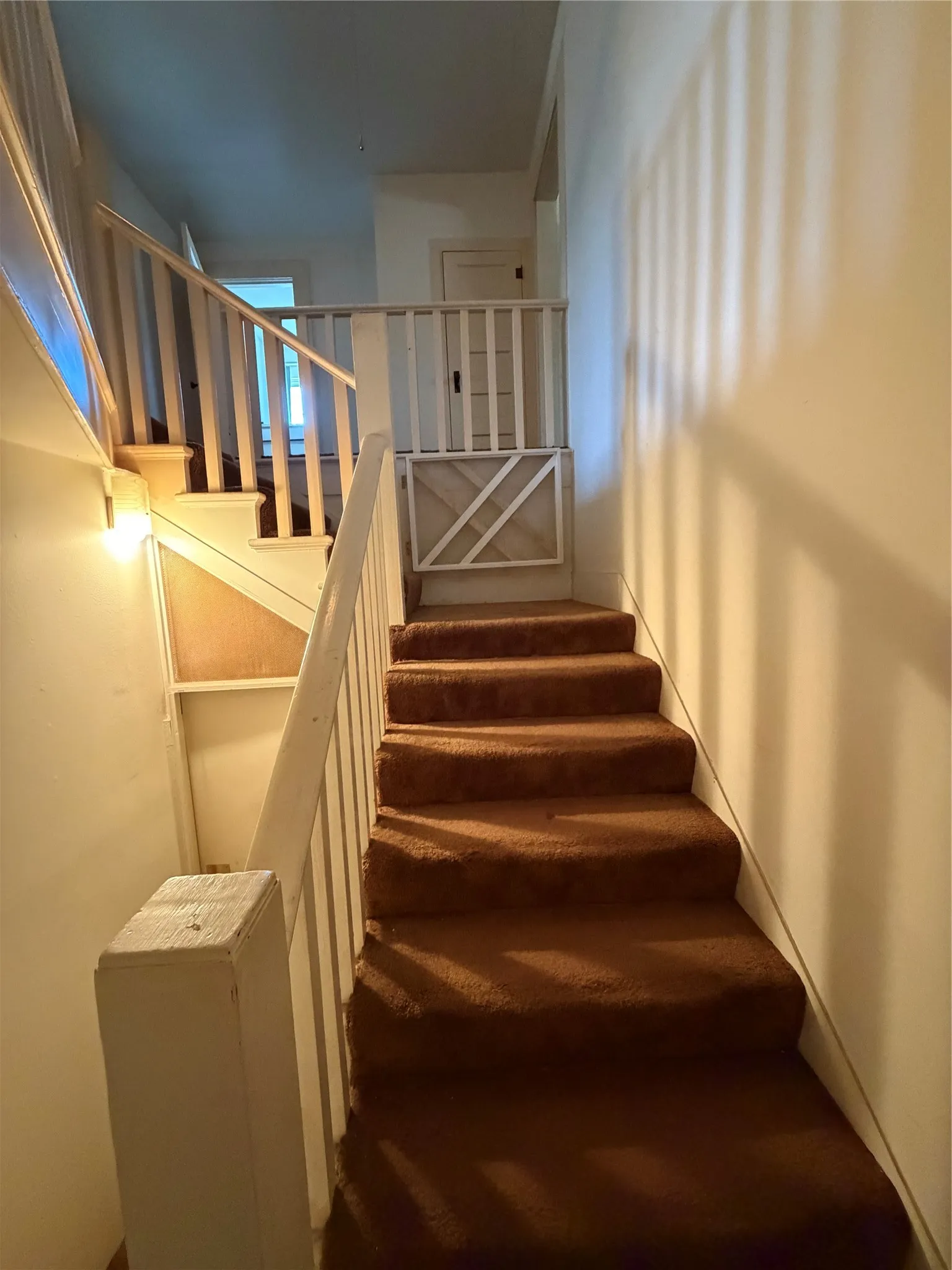 Carpeted staircase with painted wood railings and an upper landing with an interior door