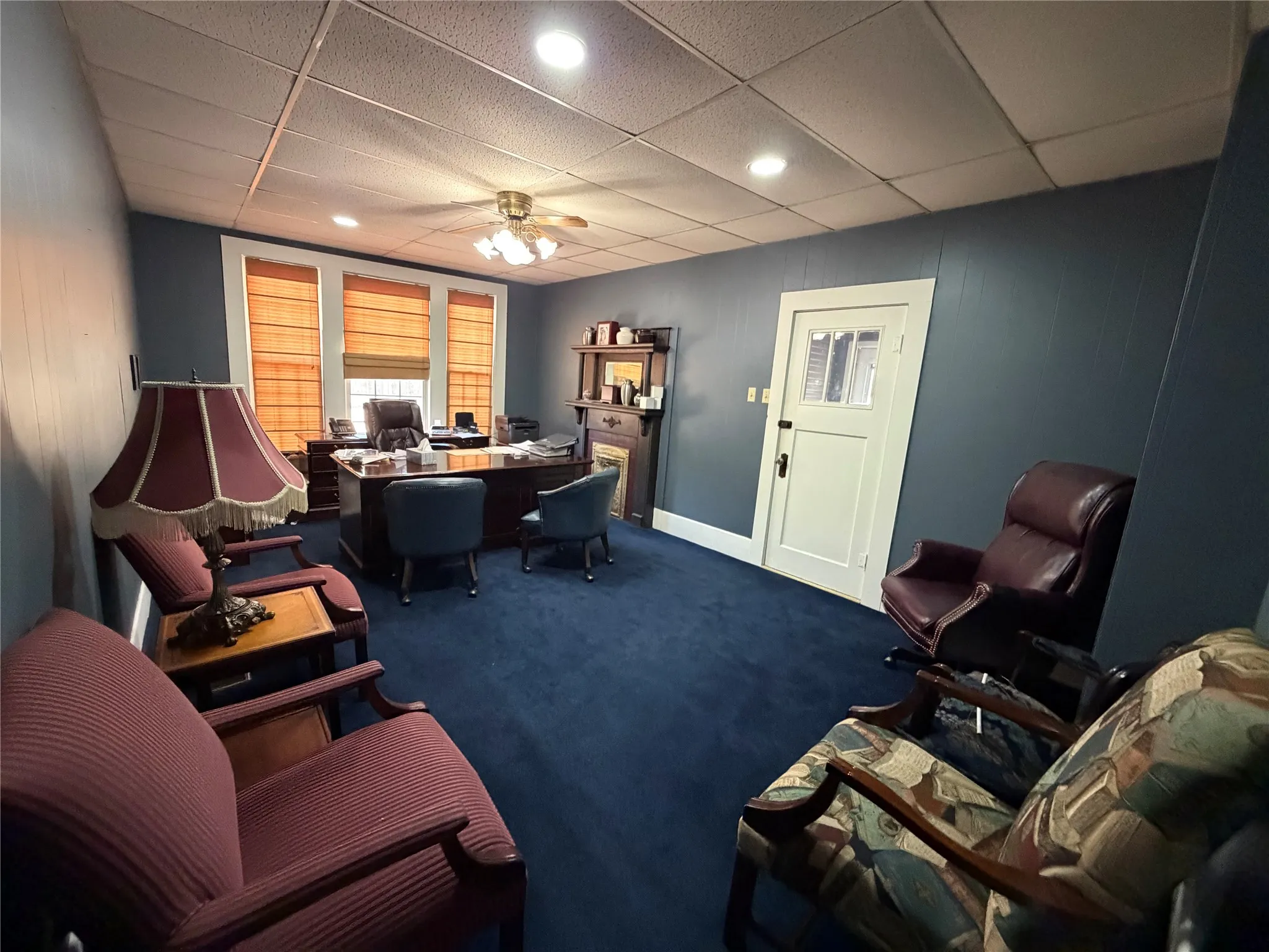 Recessed lighting, ceiling fan, three windows with blinds, paneled walls, and a white paneled door