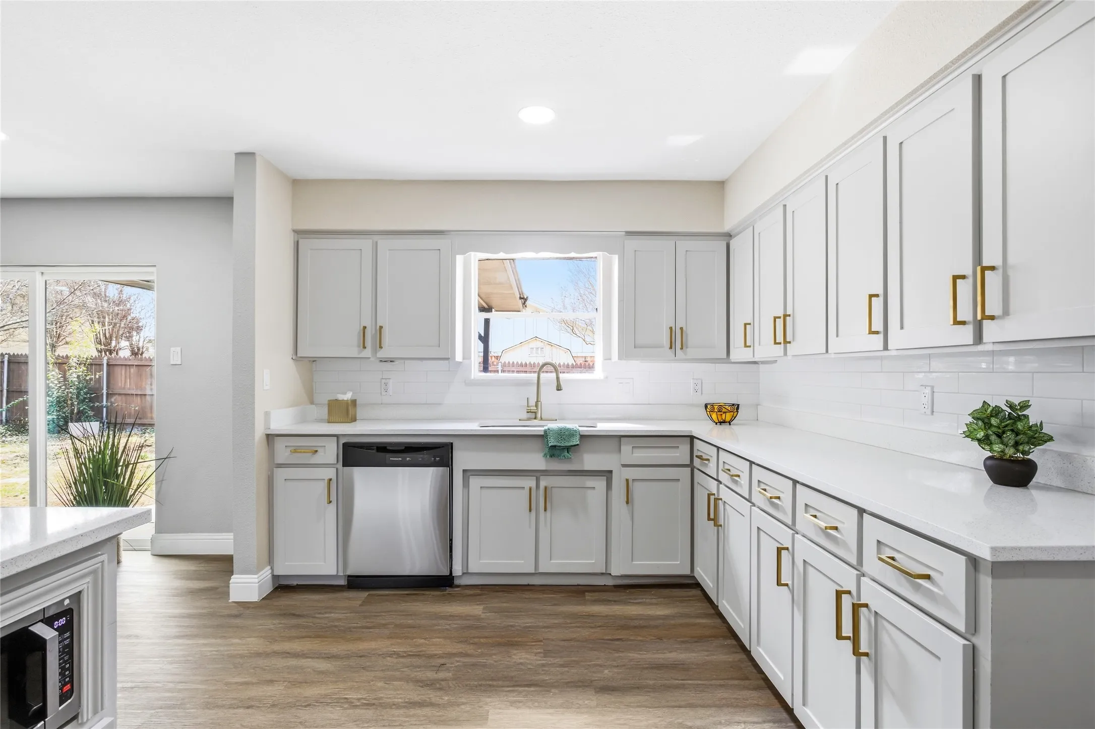 Modern kitchen featuring white shaker cabinetry, stainless steel dishwasher, white subway tile backsplash, and wood-finish flooring