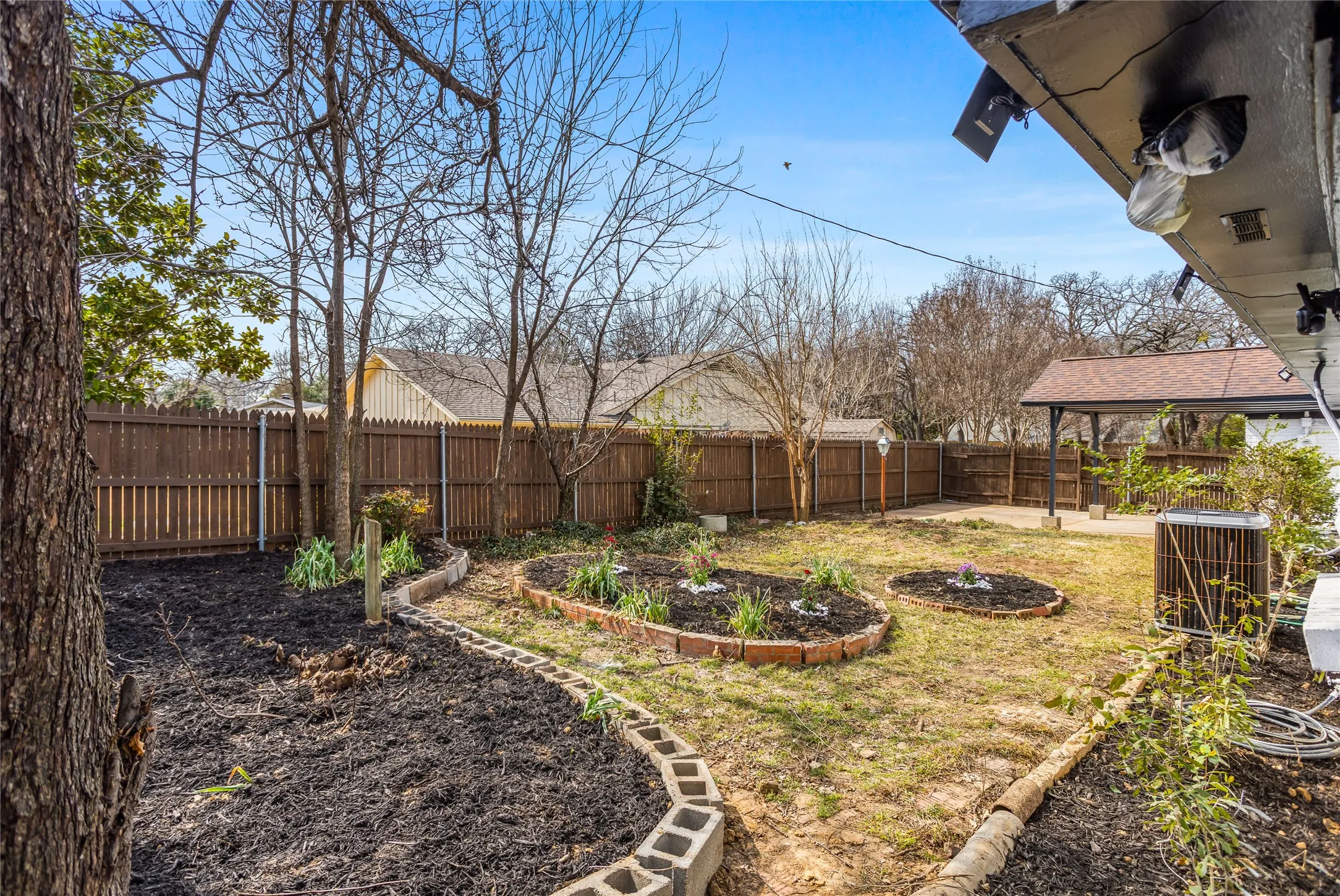 Expansive backyard featuring a wood privacy fence, established trees, and defined planting beds