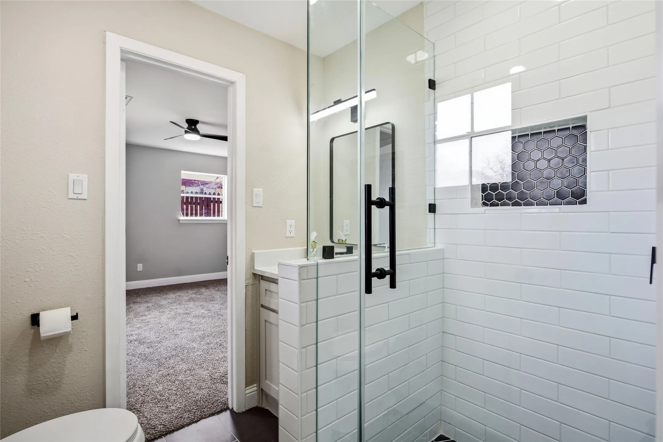 Glass-enclosed shower with subway tile surround, recessed hexagonal tile niche, and matte black fixtures