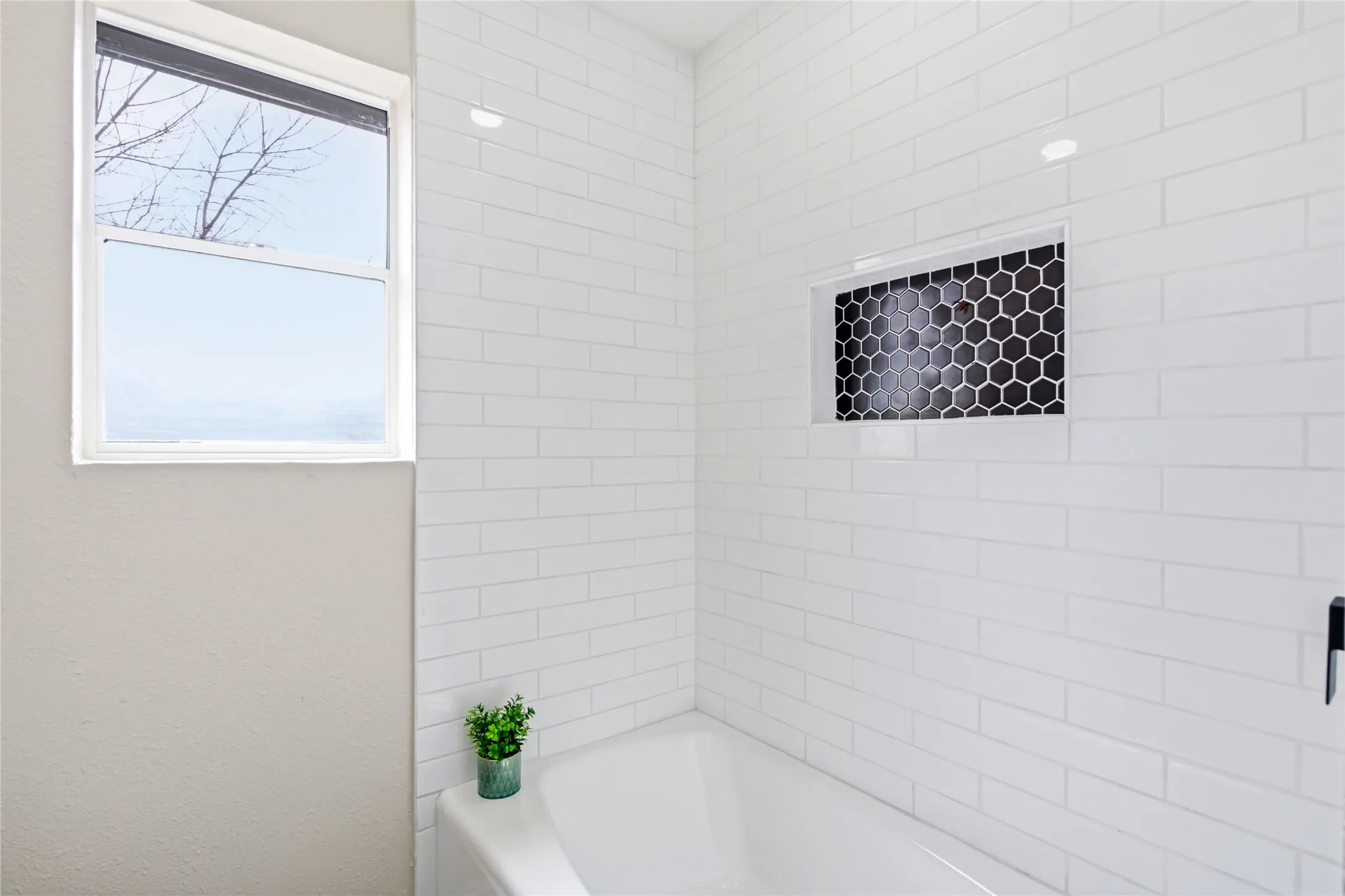 Built-in bathtub featuring a white subway tile surround, recessed niche with black hexagonal tile, and a single window