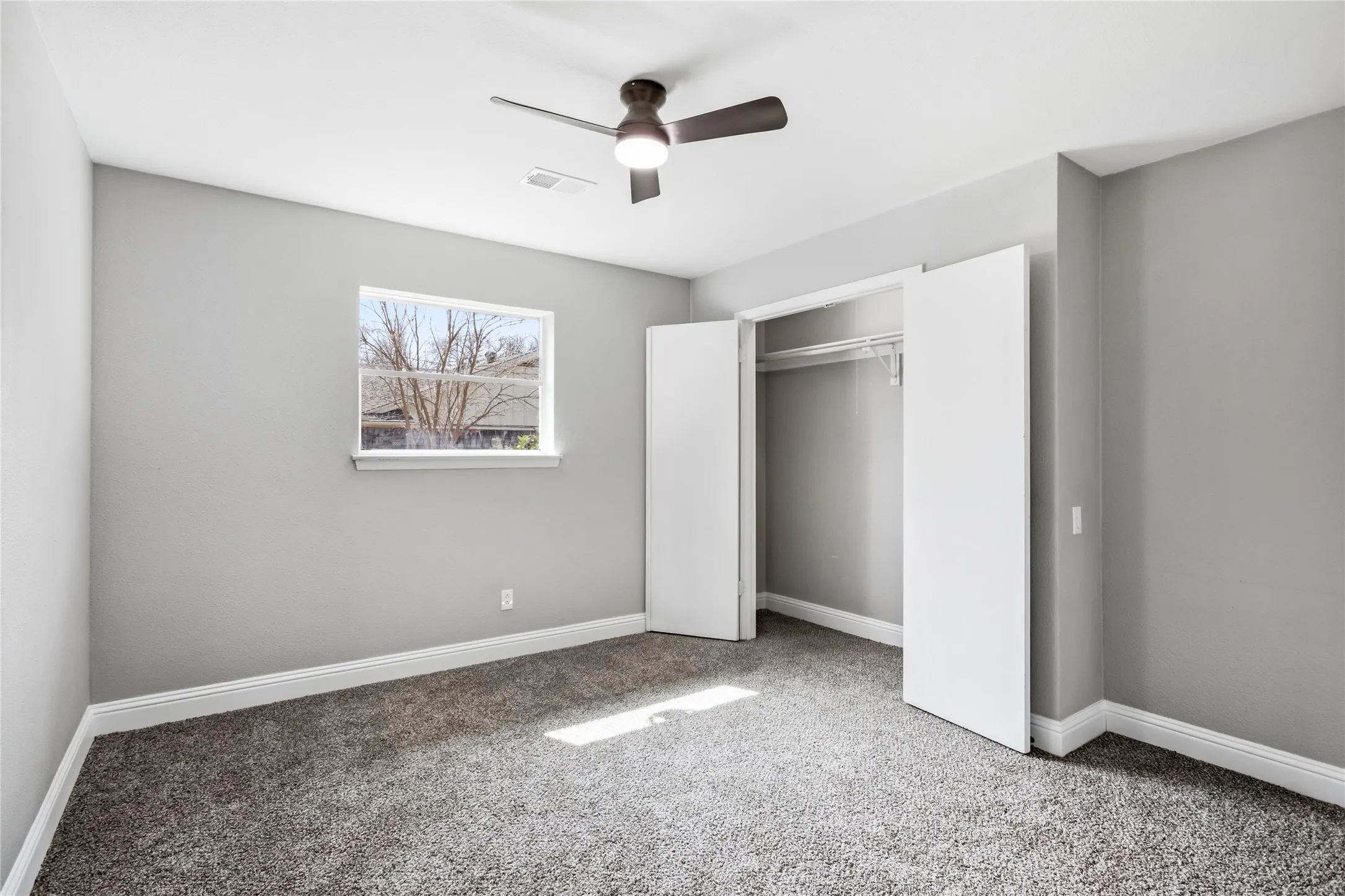 Recessed window, contemporary ceiling fan, white bi-fold closet doors, built-in closet shelving, and gray carpeting