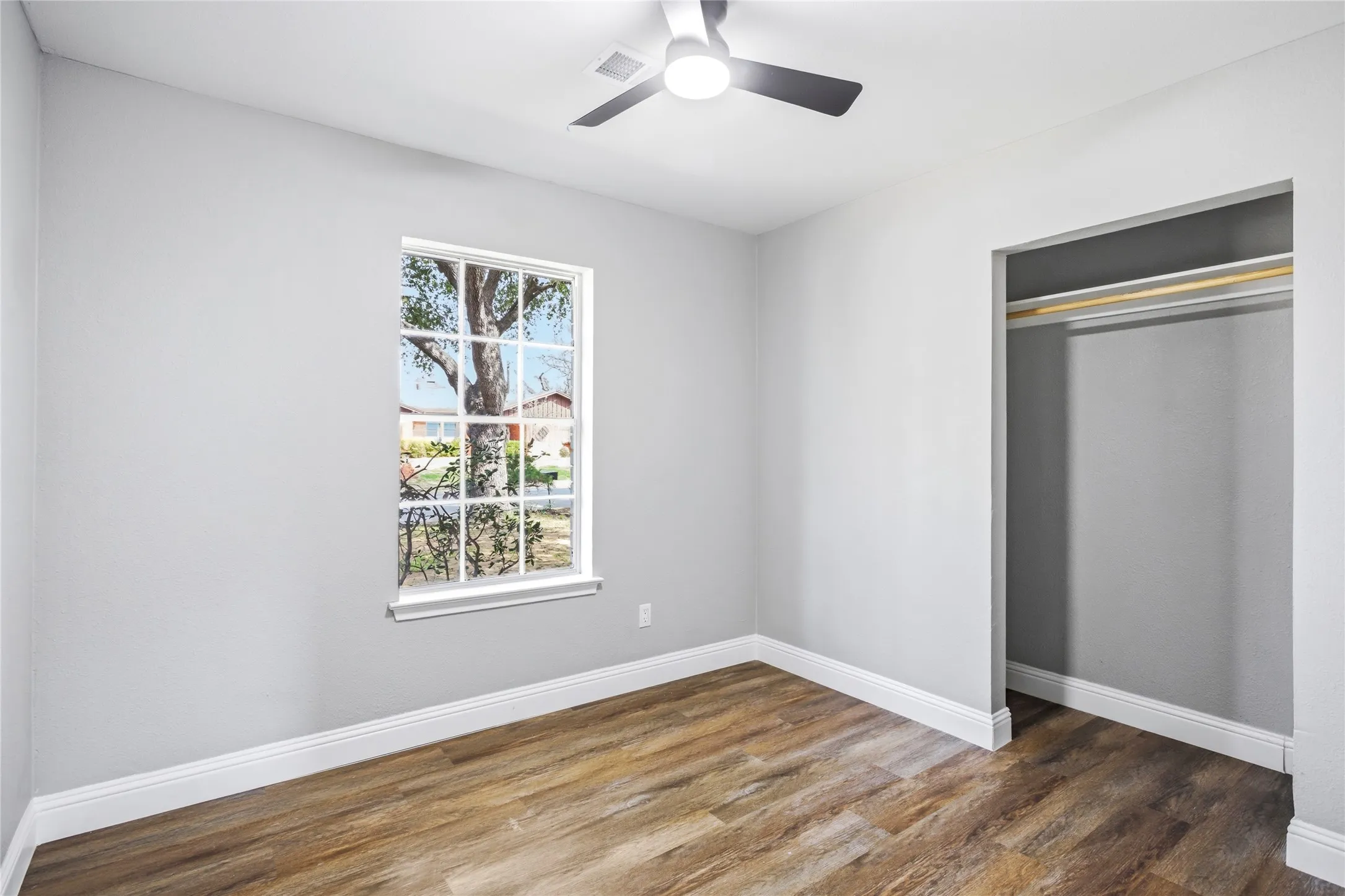 Wood-finish flooring, white trim, recessed closet, modern ceiling fan with lighting, and a window with exterior visibility