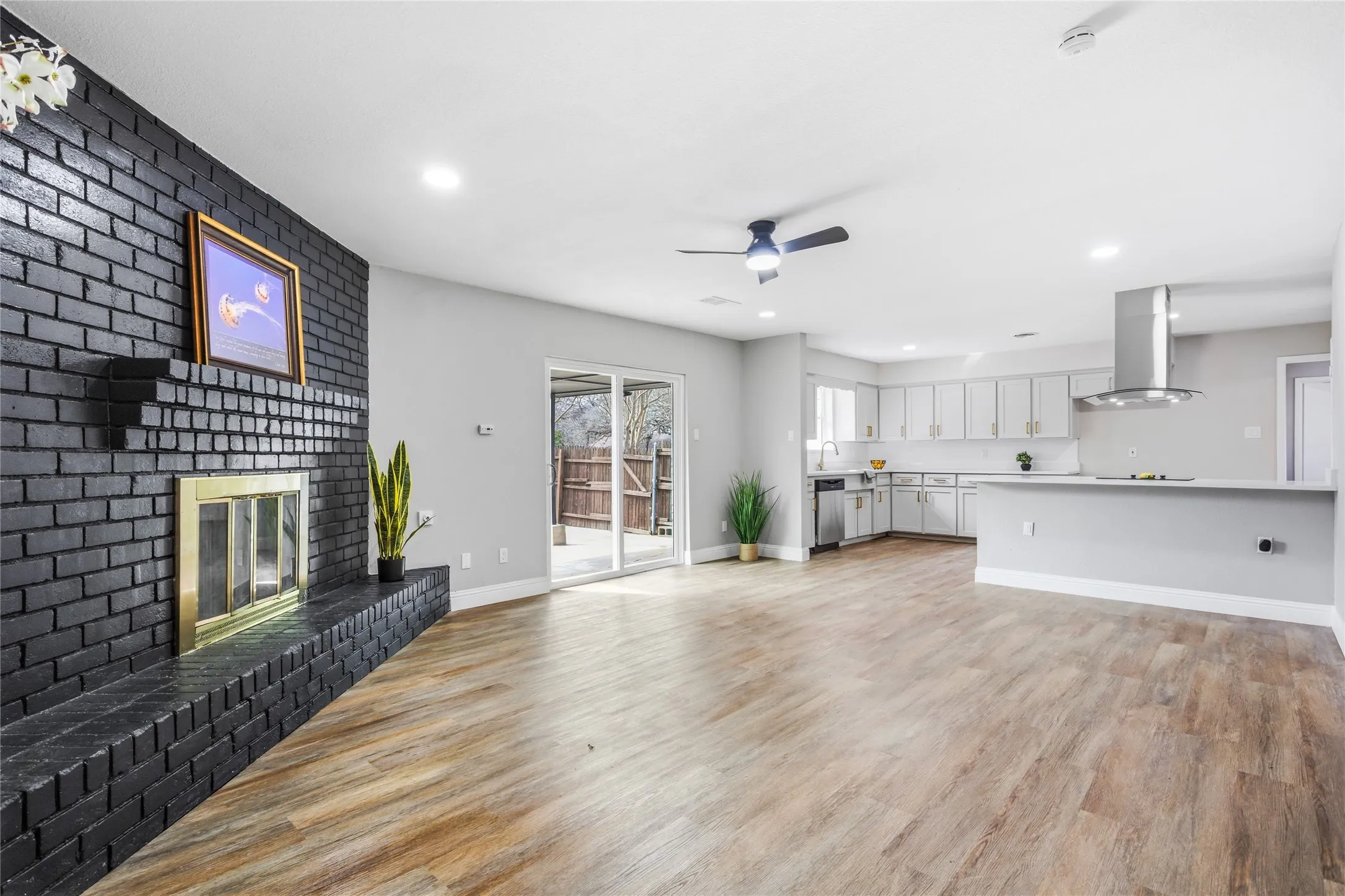 Wood-finish flooring, recessed lighting, and a black brick fireplace with a gold-tone​​‌​​​​‌​​‌‌​‌‌​​​‌‌​‌​‌​‌​​​‌​​ insert