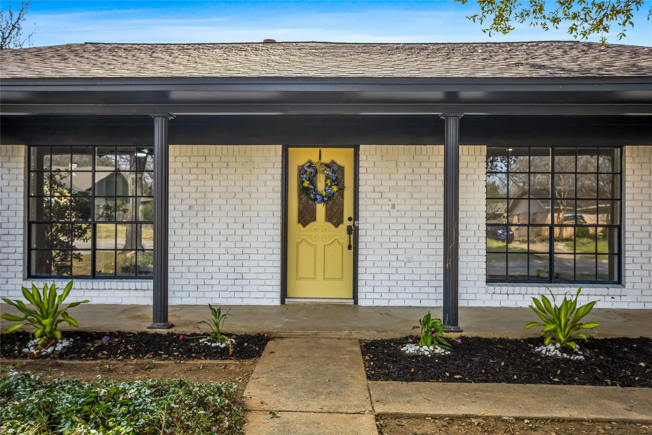 White brick exterior with a porch, black support columns, and a yellow front door