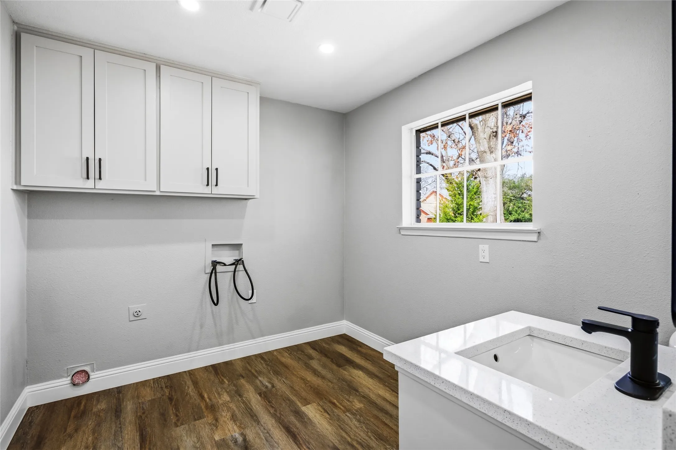 White shaker cabinetry, wood-finish flooring, single basin sink with black-finish faucet, and a large multi-pane window