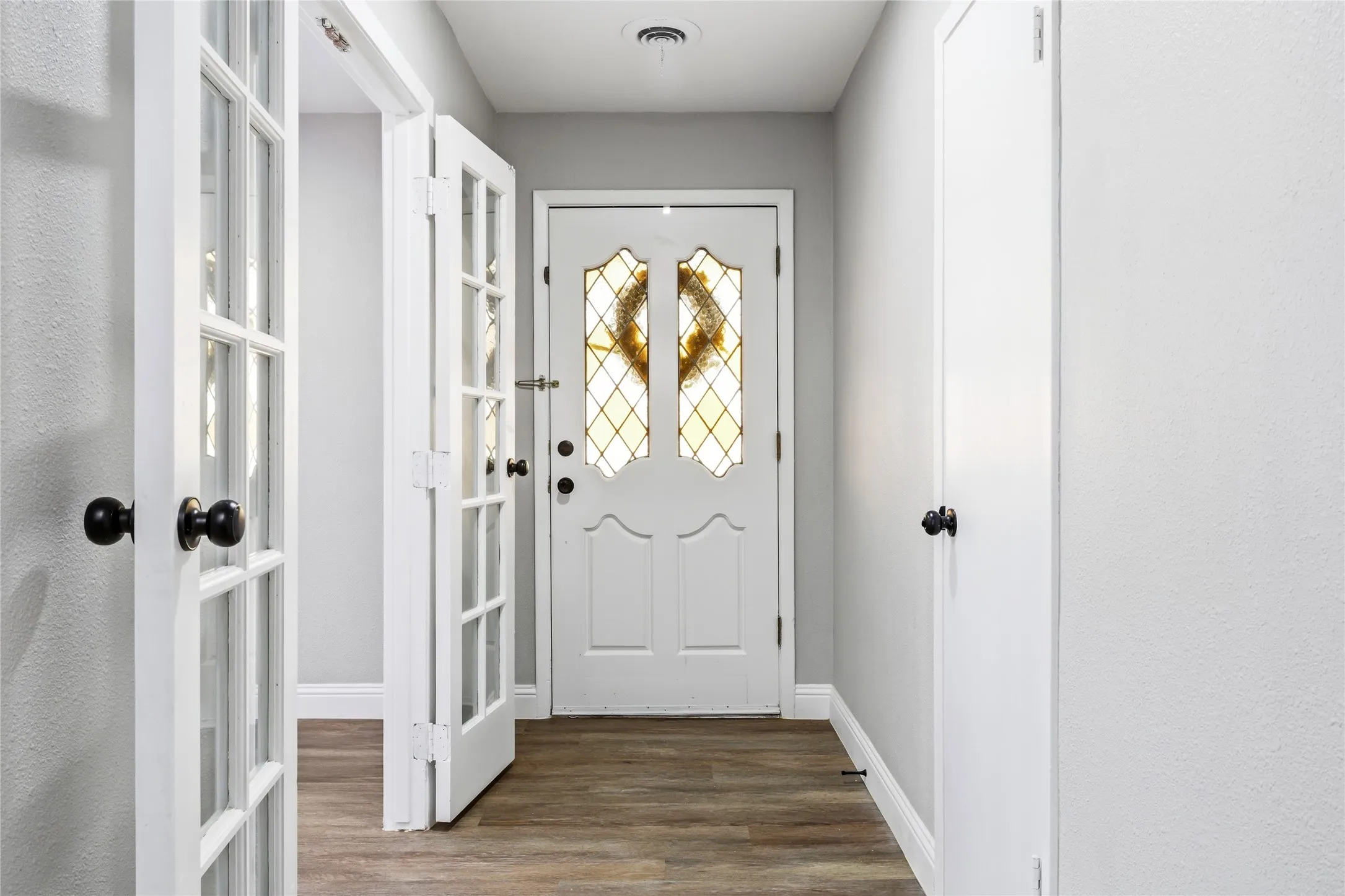 Foyer with wood-finish flooring, white paneled doors, and a decorative glass entry door with black hardware