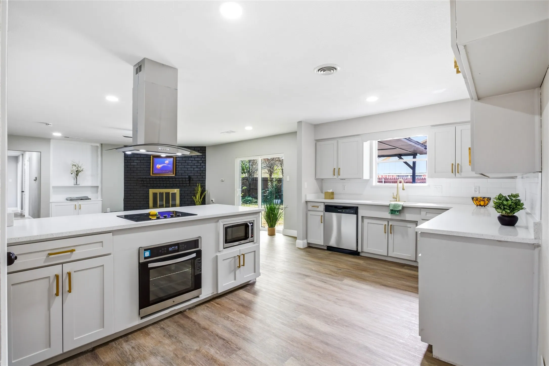 Open-concept kitchen featuring white cabinetry with gold-tone hardware, wood-finish flooring, and recessed lighting