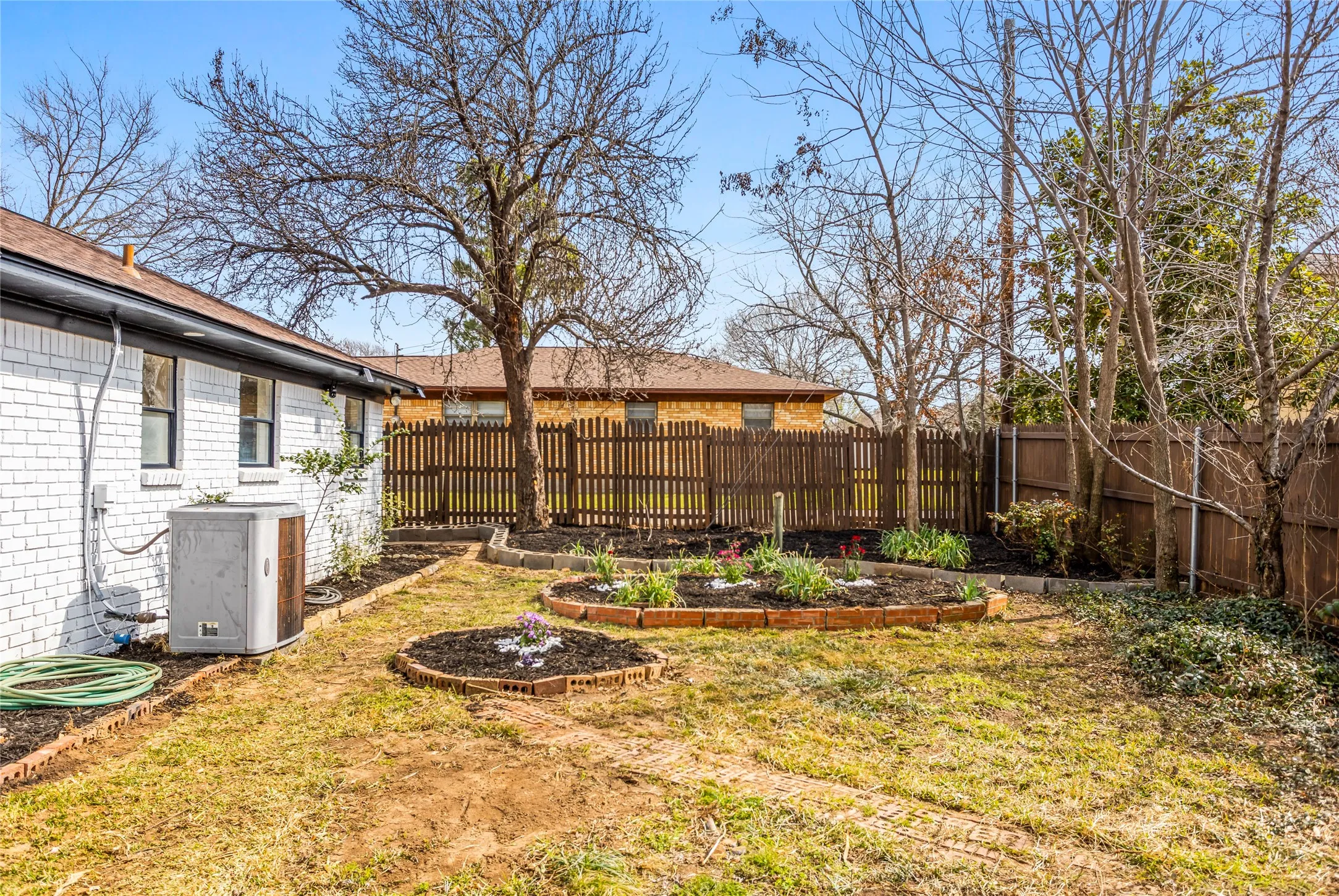 Defined backyard space with brick-edged garden beds and a wood fence perimeter