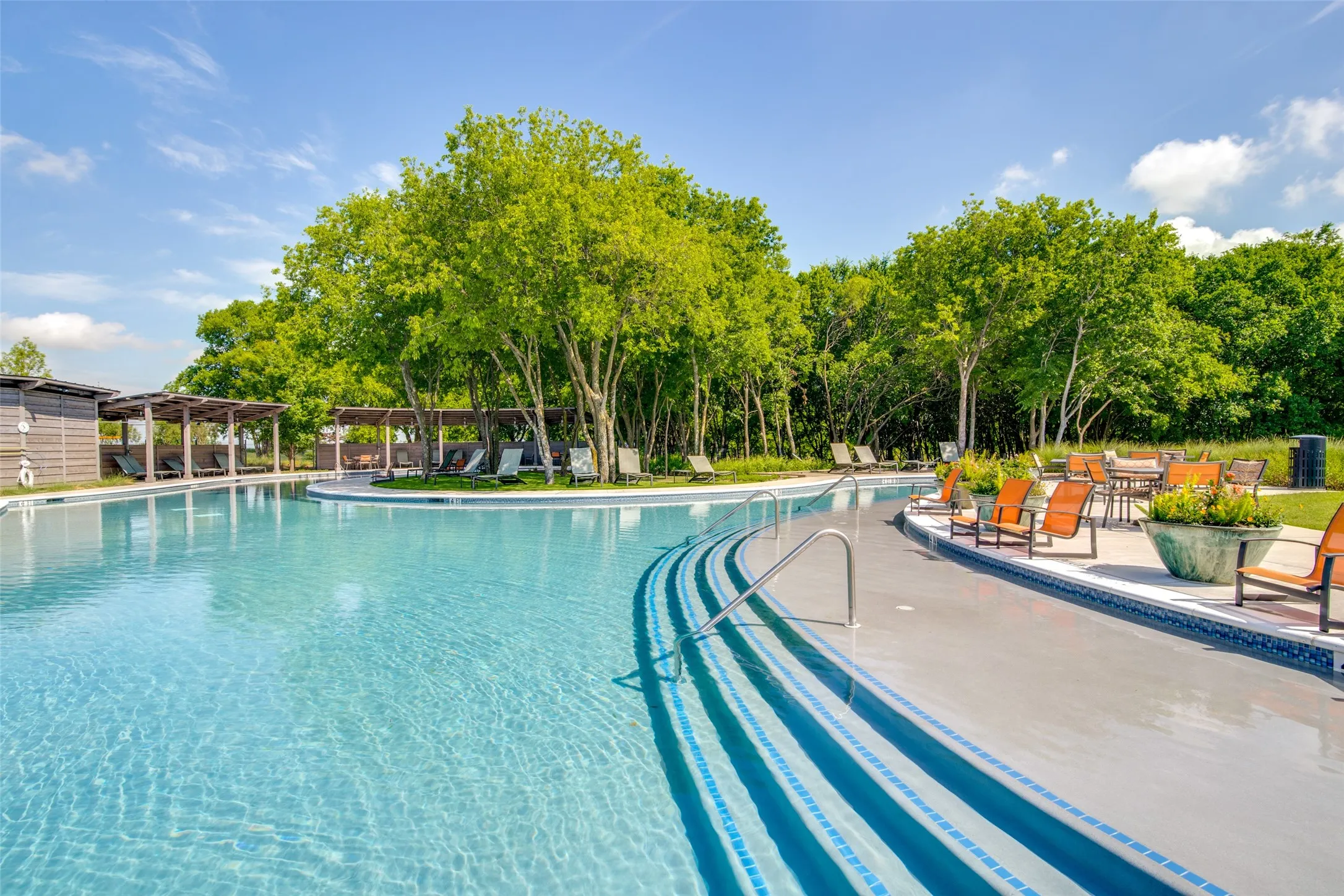 Curved swimming pool with tiled steps, surrounded by mature trees and multiple covered lounge areas