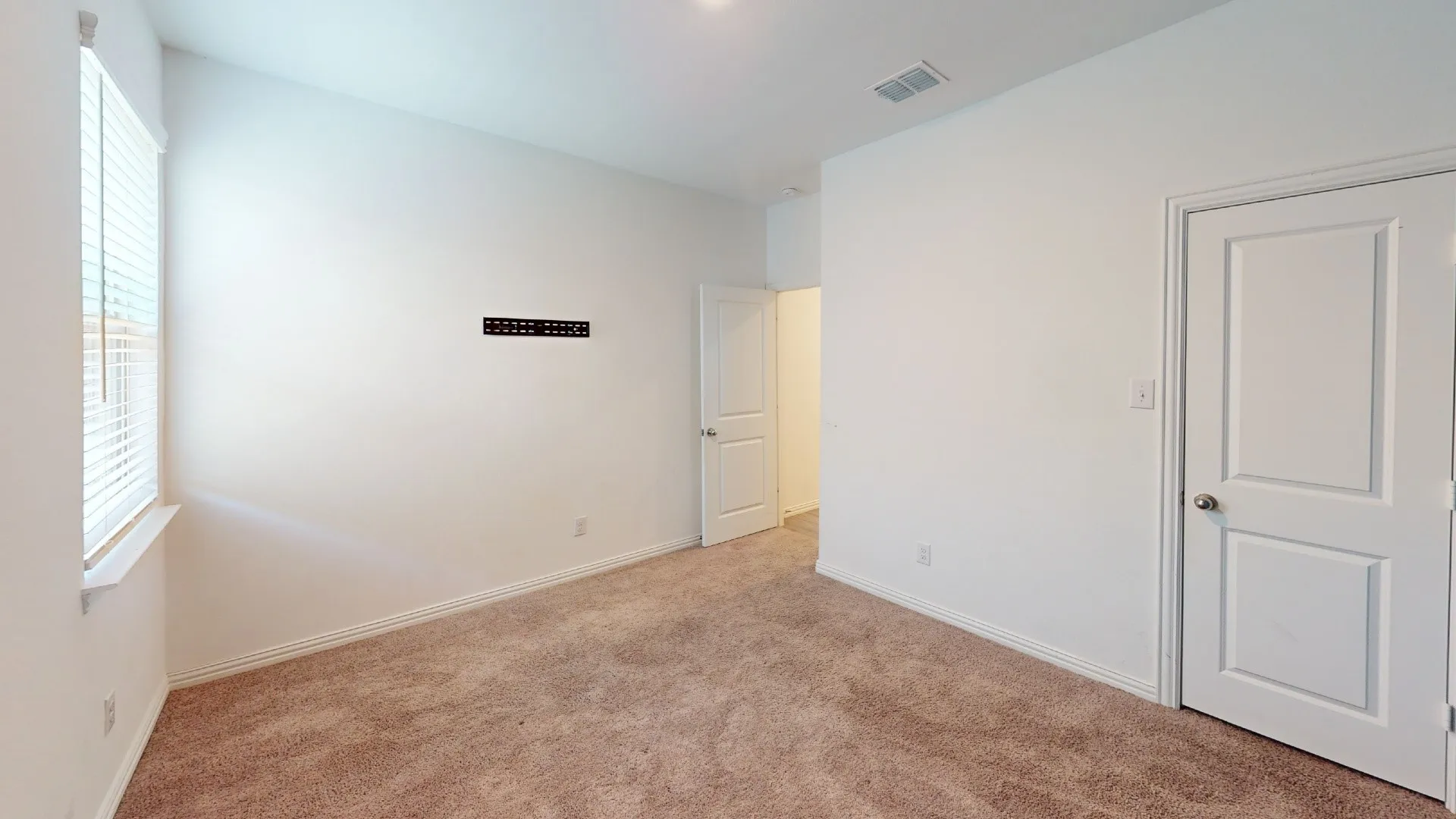 Carpeted room with white walls, a large window with blinds, and white paneled doors
