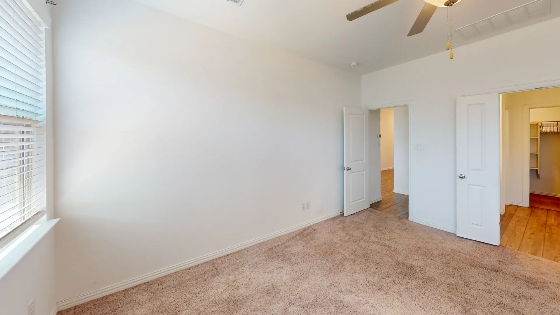 Neutral wall finishes, textured carpeting, a window with blinds, and a ceiling fan
