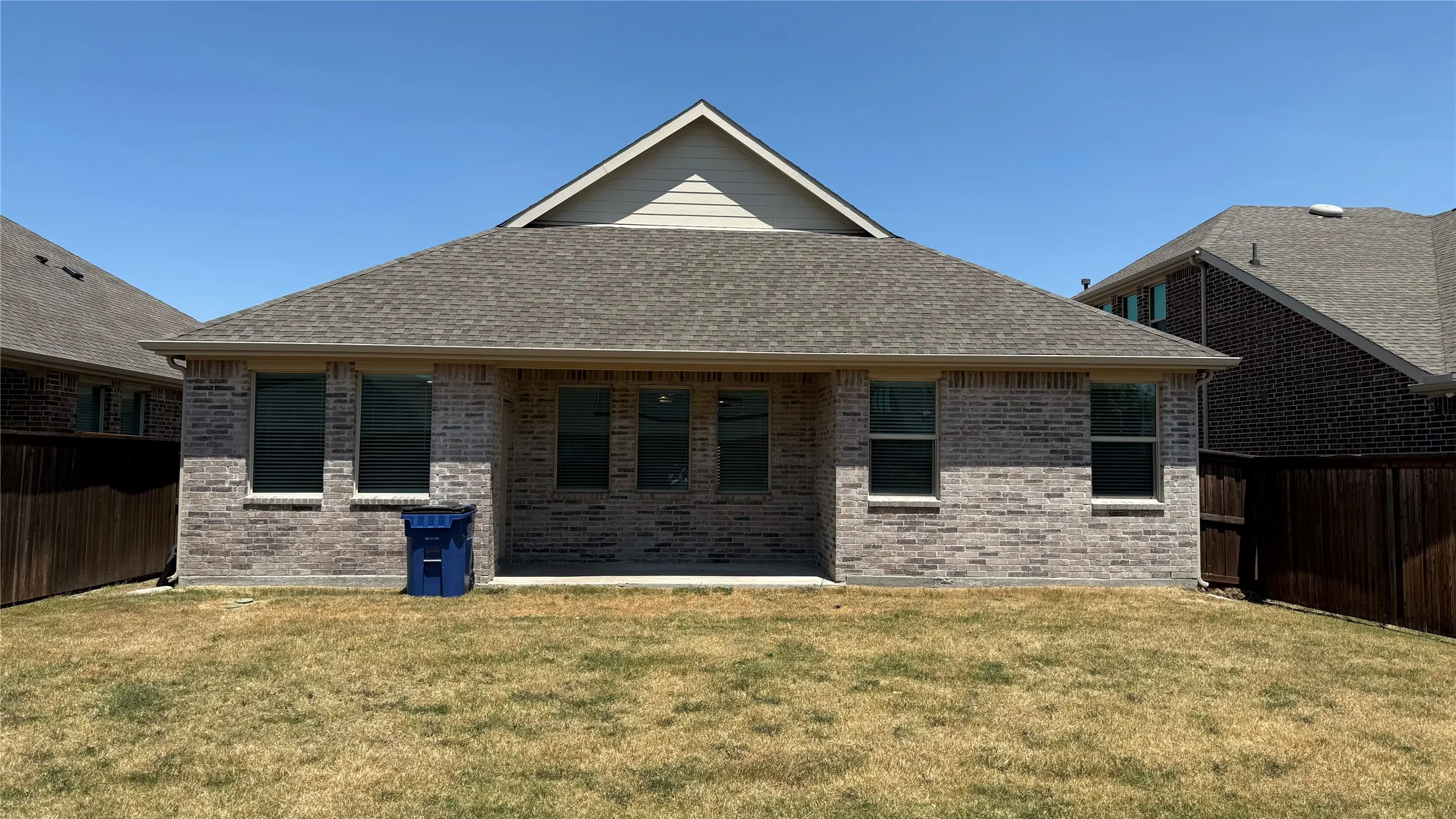 Brick exterior with a covered patio, multiple windows, and a shingled roof
